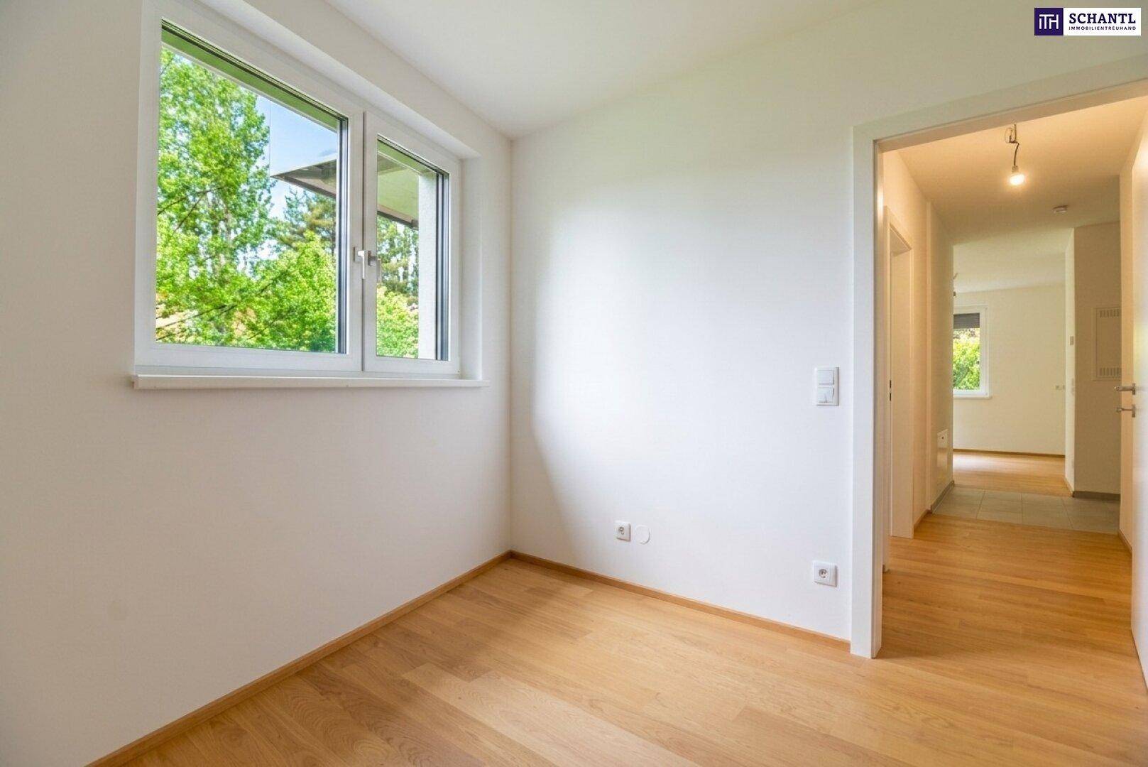 Helles Schlafzimmer mit Holzboden und Fenster, das einen Blick ins Grüne bietet.