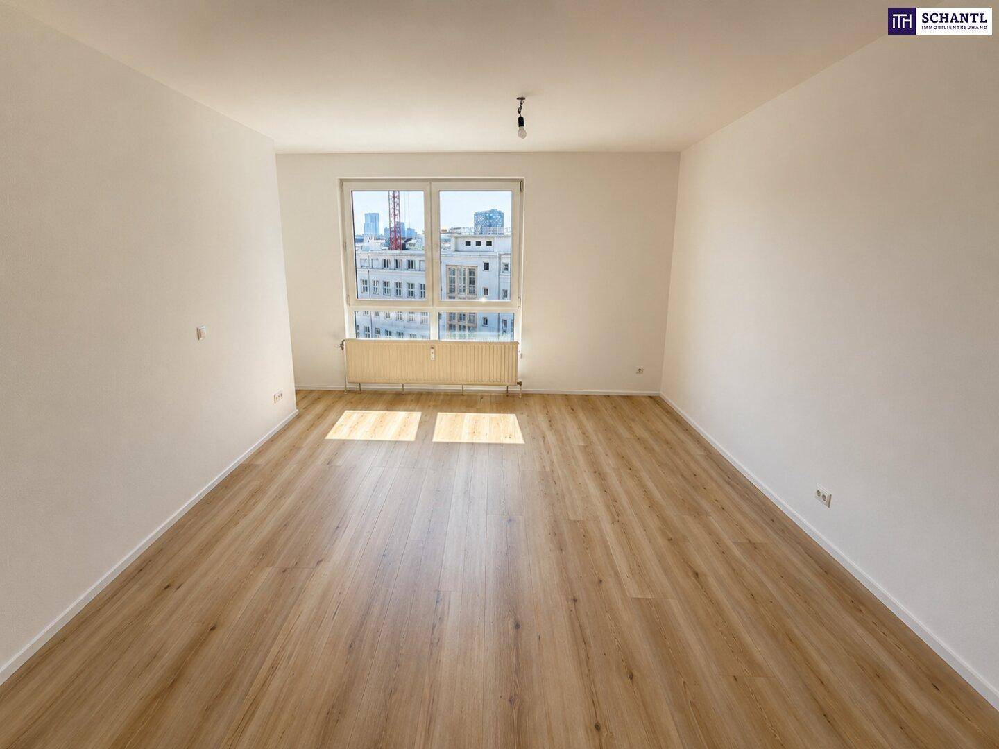 Geräumiges, helles Zimmer mit Laminatboden, weißen Wänden und einem Fenster mit Stadtblick.