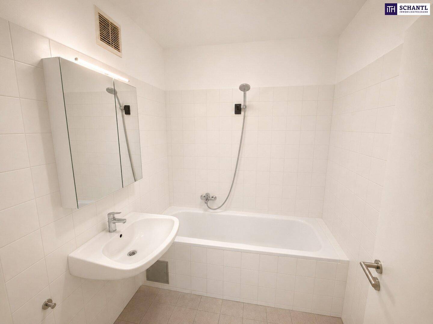 Helles Badezimmer mit weißen Fliesen, Badewanne mit Duschfunktion und einem Waschbecken.
