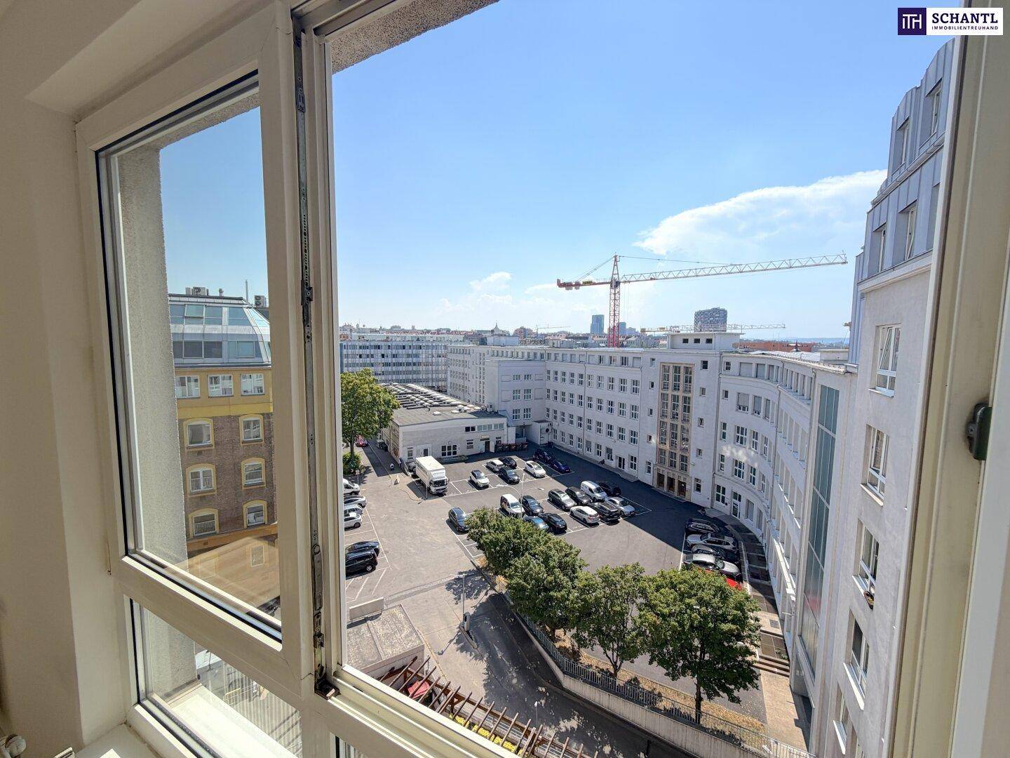 Blick aus dem Fenster auf einen städtischen Innenhof mit parkenden Autos und umliegenden Gebäuden.
