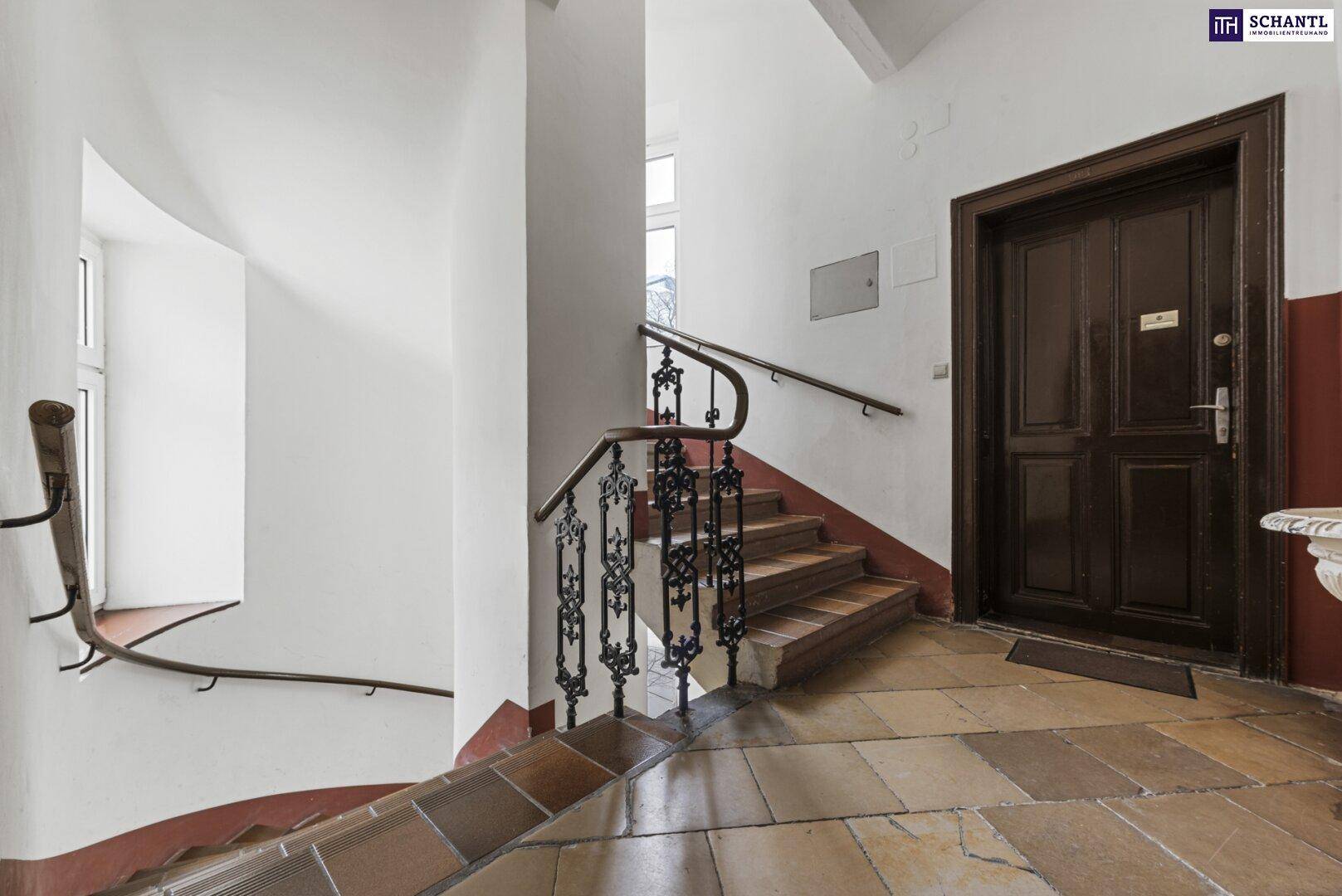 Historisches Treppenhaus mit schmiedeeisernem Geländer, Holzstufen und gefliestem Boden.