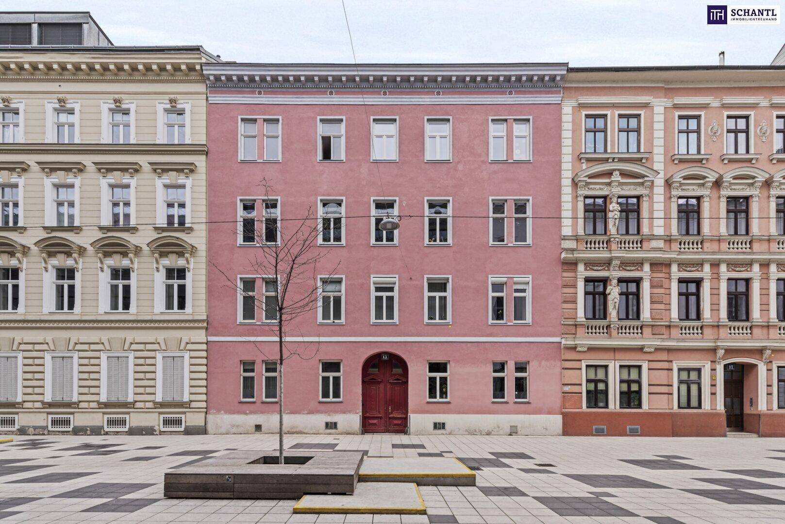 Historische Fassade eines rosafarbenen Gebäudes in einer belebten Stadtumgebung.