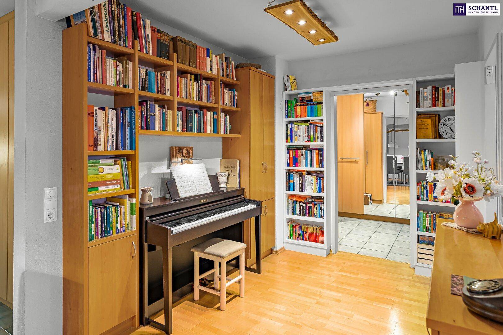 Arbeitsbereich mit Klavier, Bücherregalen und Holzboden, offen zu einem weiteren Raum.