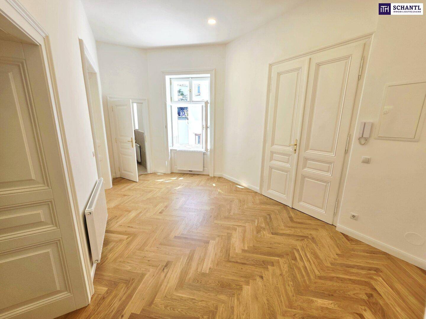 Geräumiger, heller Raum mit Fischgrätparkett und hohen Türen, ideal für ein Wohnzimmer.