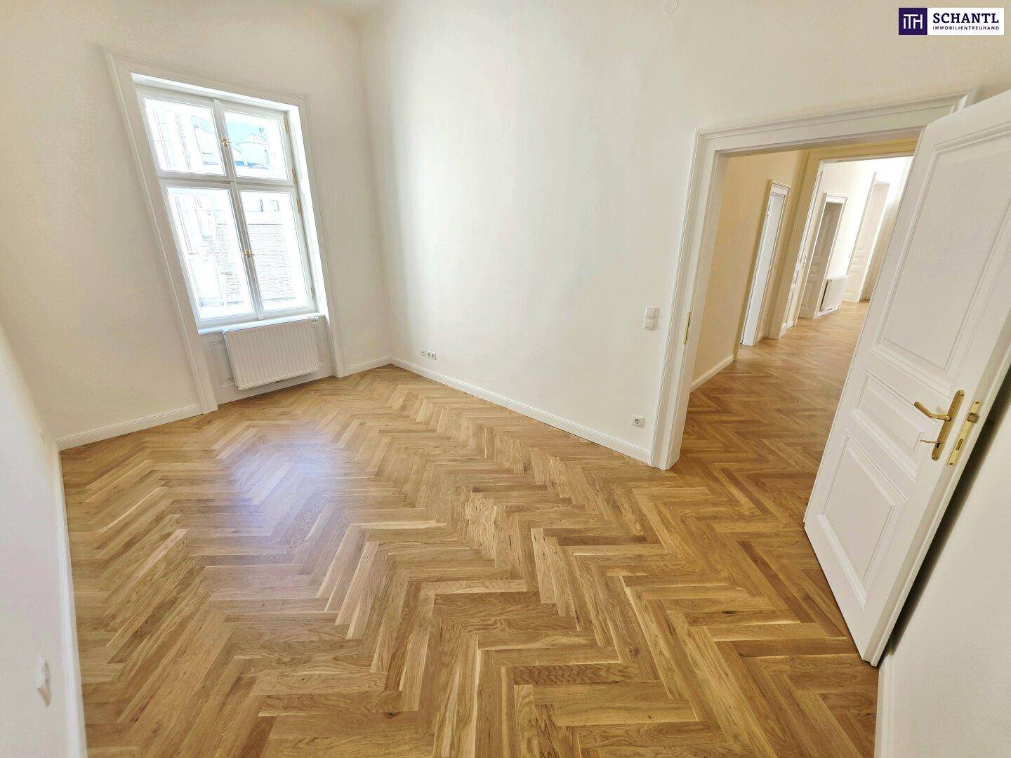 Geräumiges Zimmer mit Fischgrätparkett und hohen Fenstern, das viel Tageslicht hereinlässt.