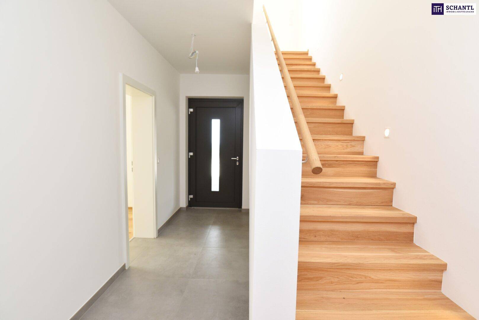 Eingangsbereich mit moderner Holztreppe und dunkler Eingangstür, die zu den oberen Etagen führt.