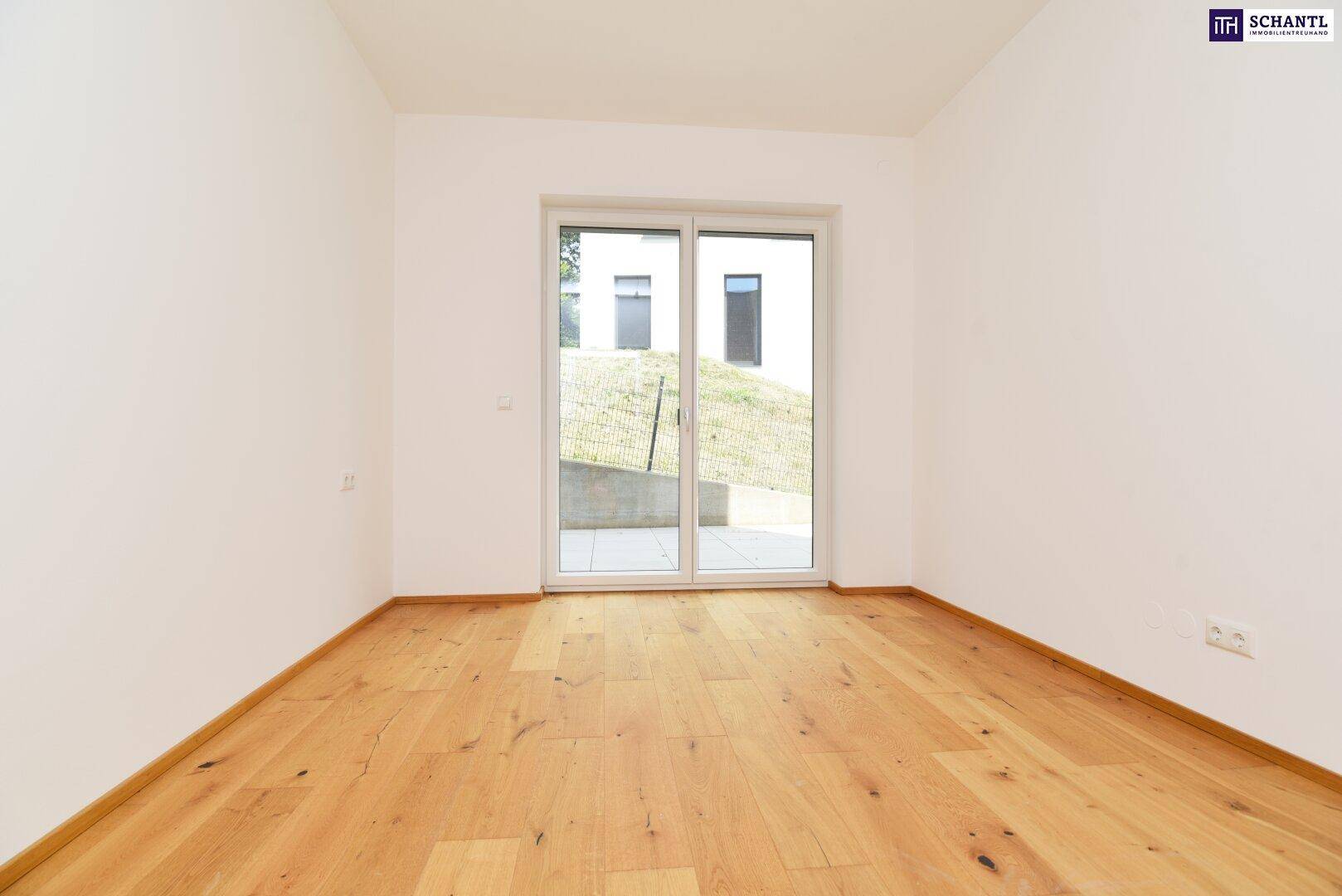 Helles Zimmer mit Holzboden und großer Fenstertür, die Zugang nach draußen bietet.