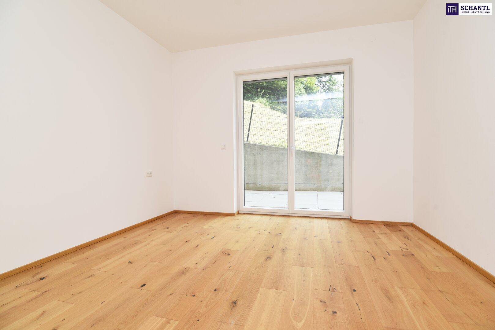 Leeres Zimmer mit hellem Parkettboden und Zugang zu einem Außenbereich durch eine große Fenstertür.