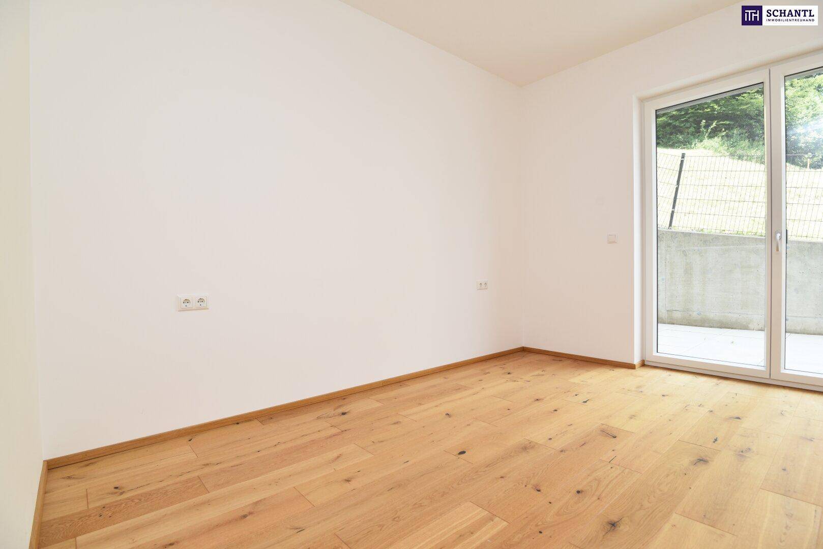 Leeres Zimmer mit Holzboden und großem Fenster, das viel Licht in den Raum bringt.