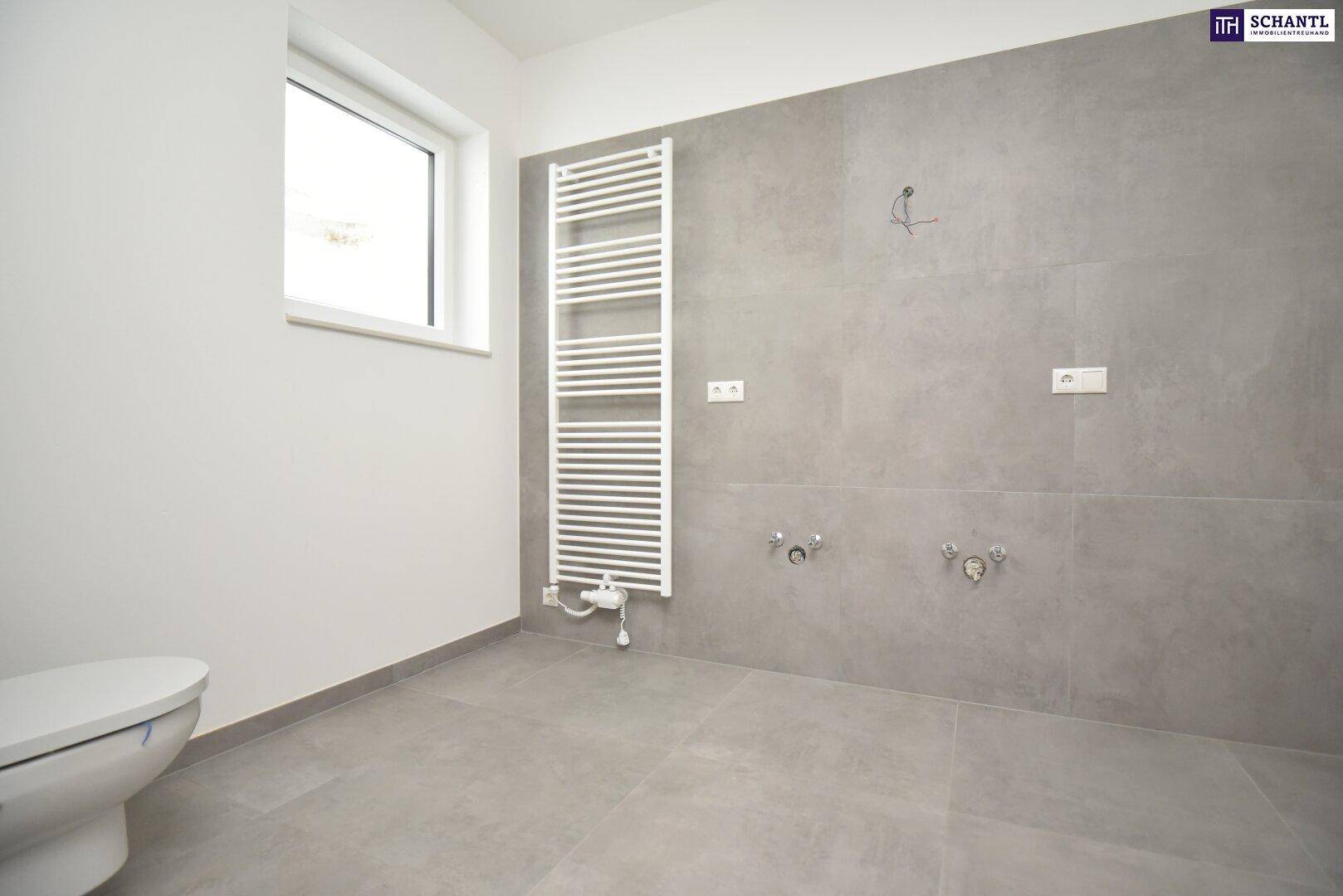 Modernes Badezimmer im Rohbau mit grauen Fliesen, Fenster und Handtuchheizkörper.