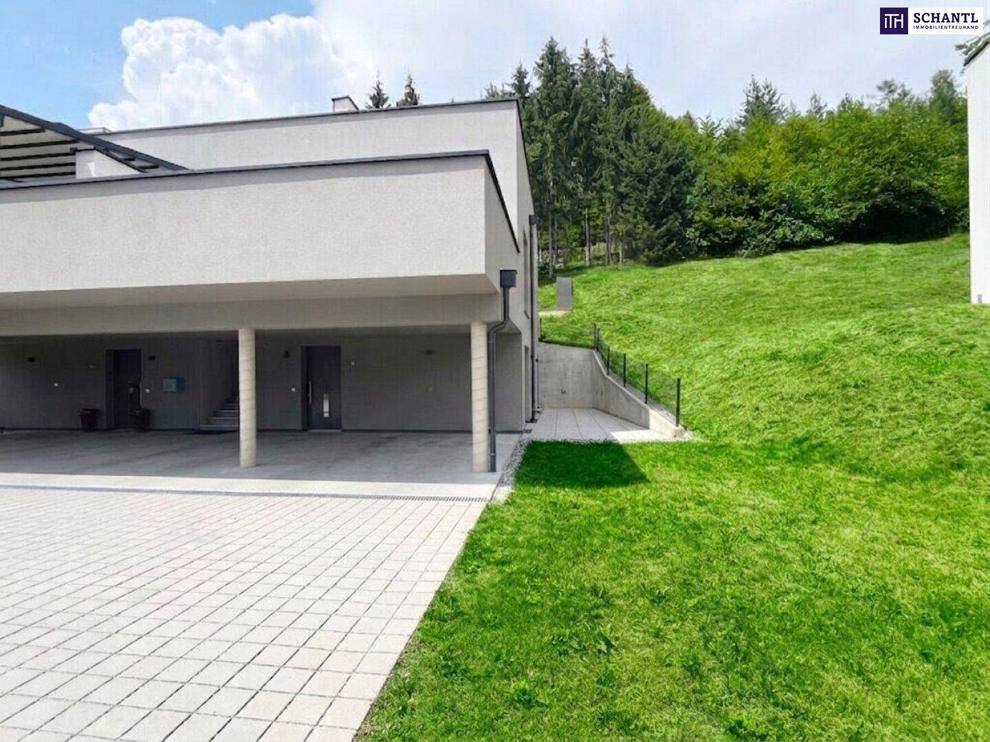 Modernes Gebäude mit Carport und Grünfläche am Hang, umgeben von Bäumen.