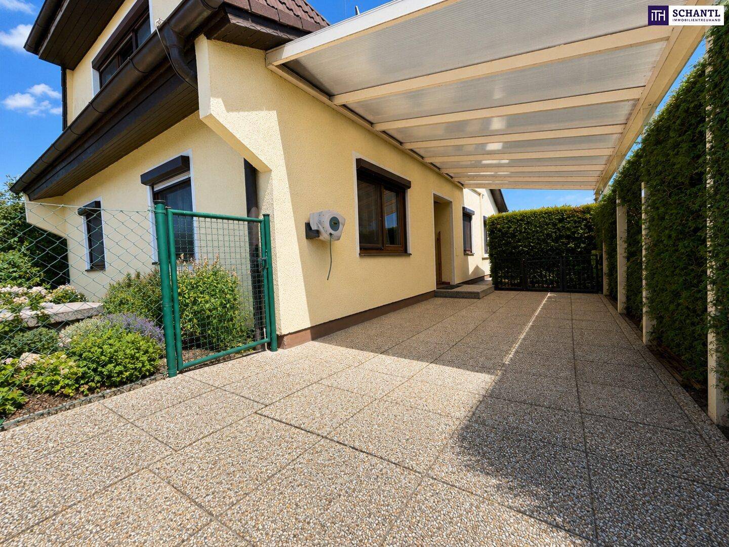 Überdachter Carport-Bereich mit gepflasterter Einfahrt neben dem Haus.