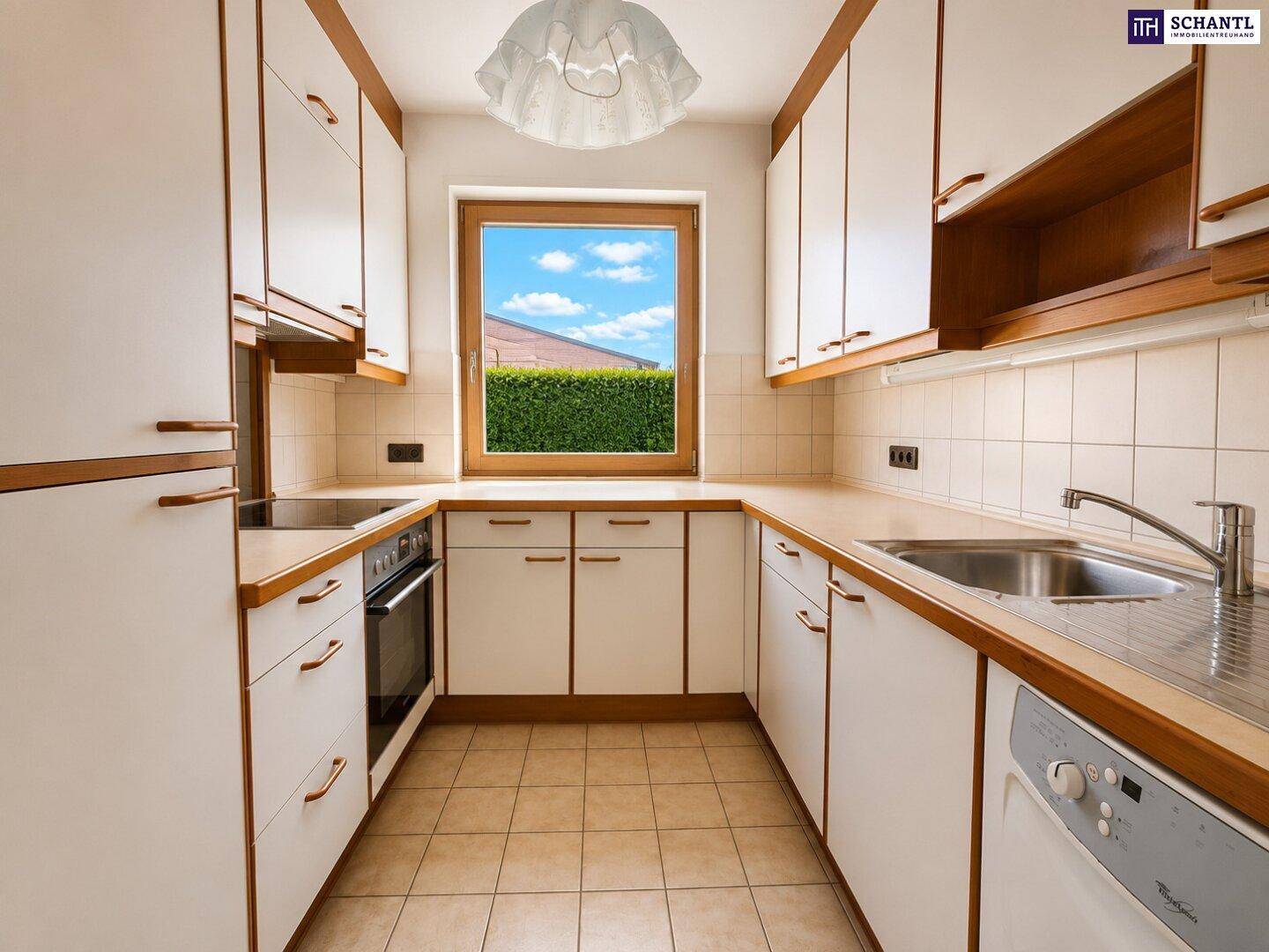 Funktionale Küche mit weißen Schränken, Holzdetails und Fensterblick ins Grüne.
