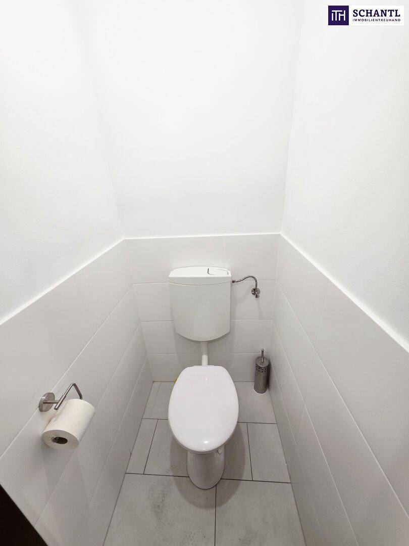 Saubere Toilette in einem kleinen Raum mit weißen Fliesen und einem Spülkasten.