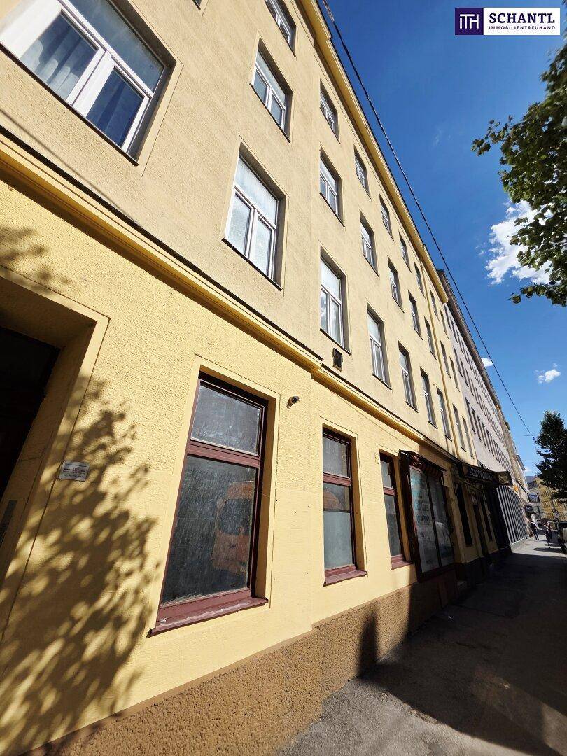 Seitenansicht des Gebäudes mit gelber Fassade und großen Fenstern im Erdgeschoss, die zur Straße zeigen.