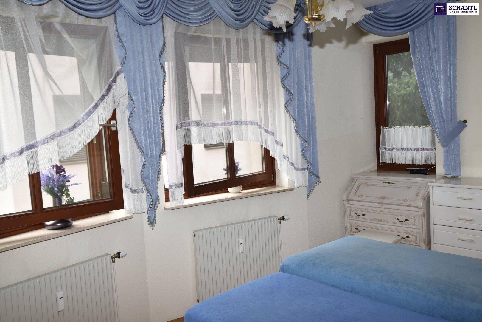 Helles Schlafzimmer mit zwei Betten, blauen Vorhängen und Fenstern, die viel Licht hereinlassen.