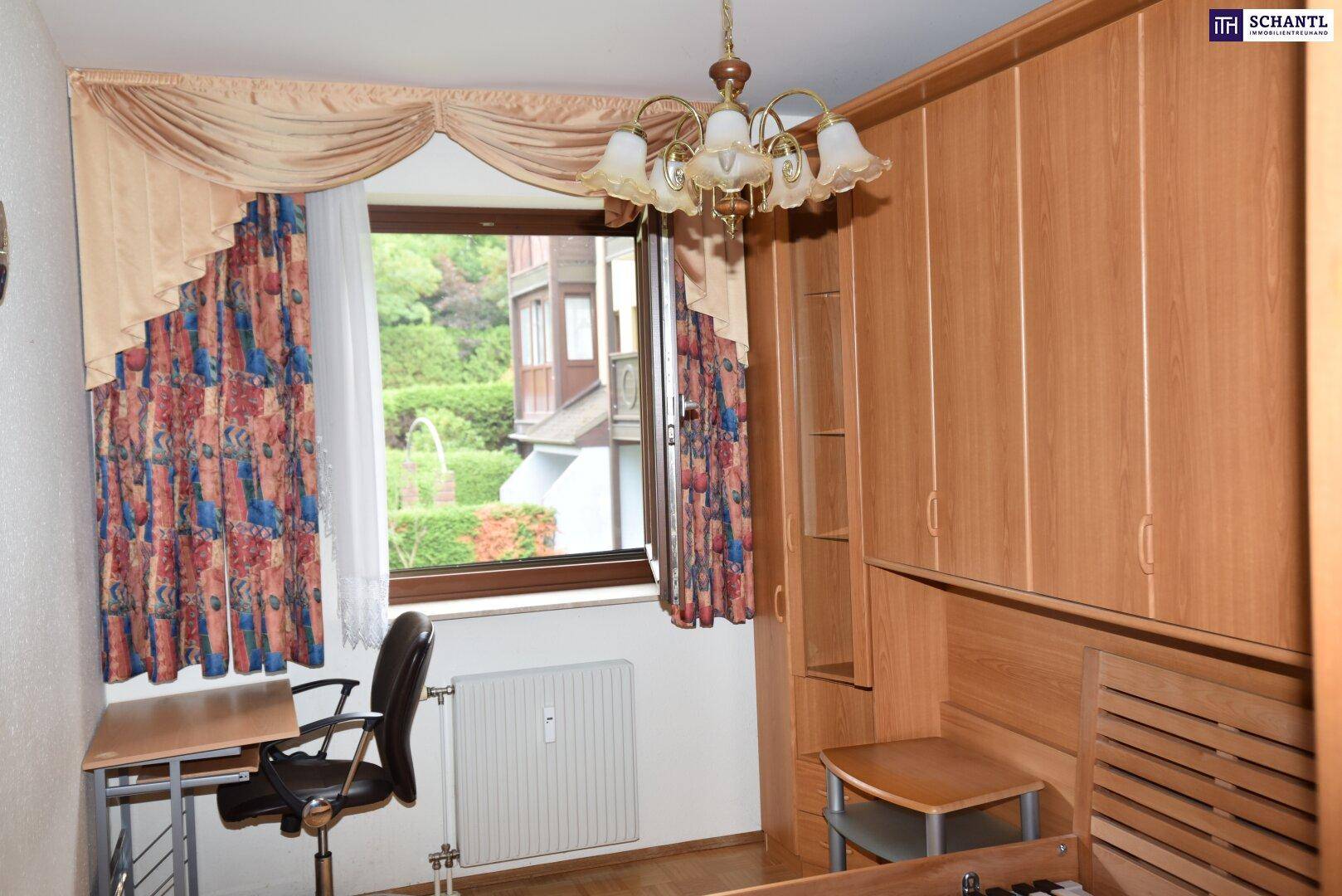 Schlafzimmer mit integrierten Holzschränken, Schreibtisch und Fenster mit Blick ins Grüne.
