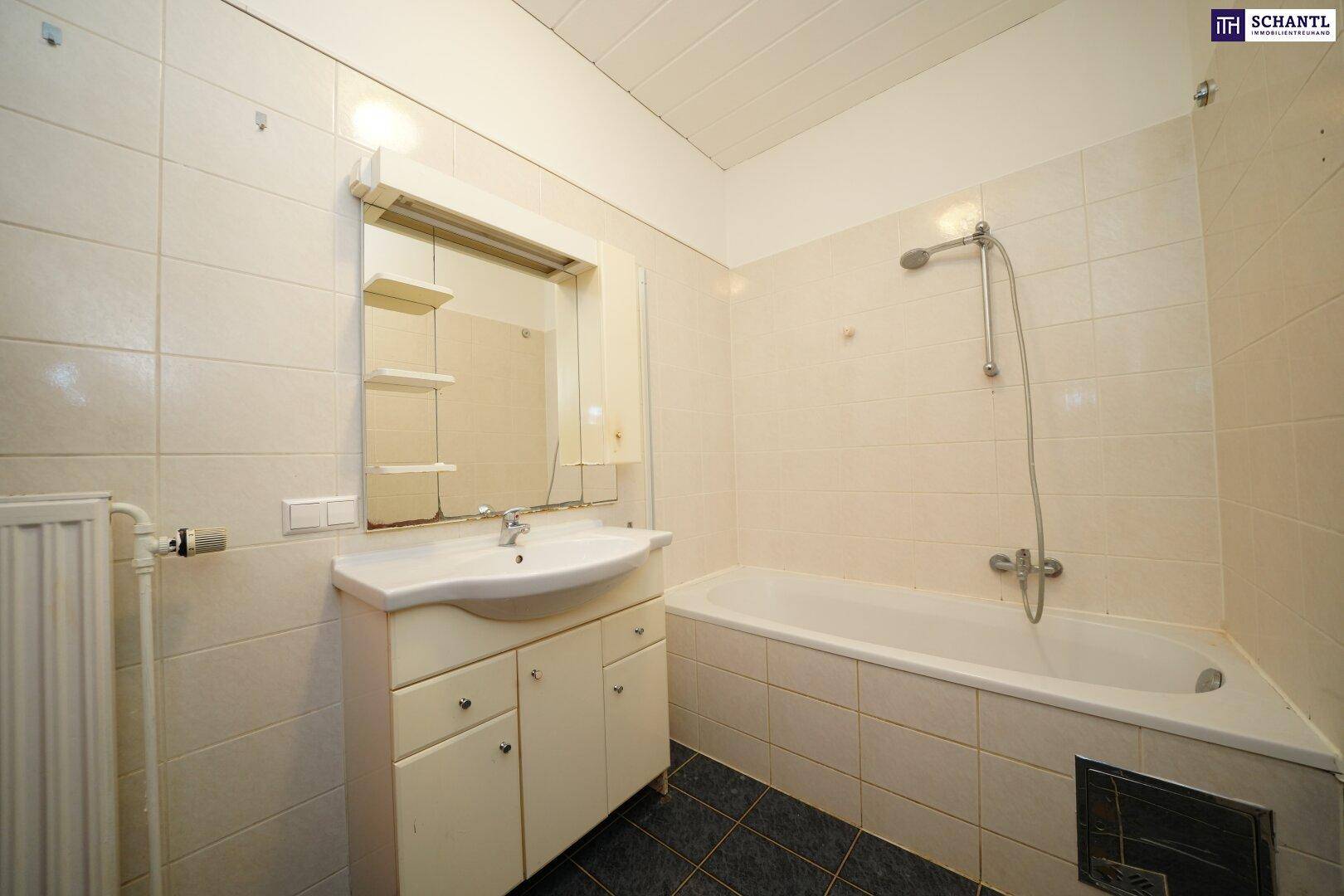 Badezimmer mit Badewanne, Waschbecken und Spiegel, komplett gefliest und funktional ausgestattet.