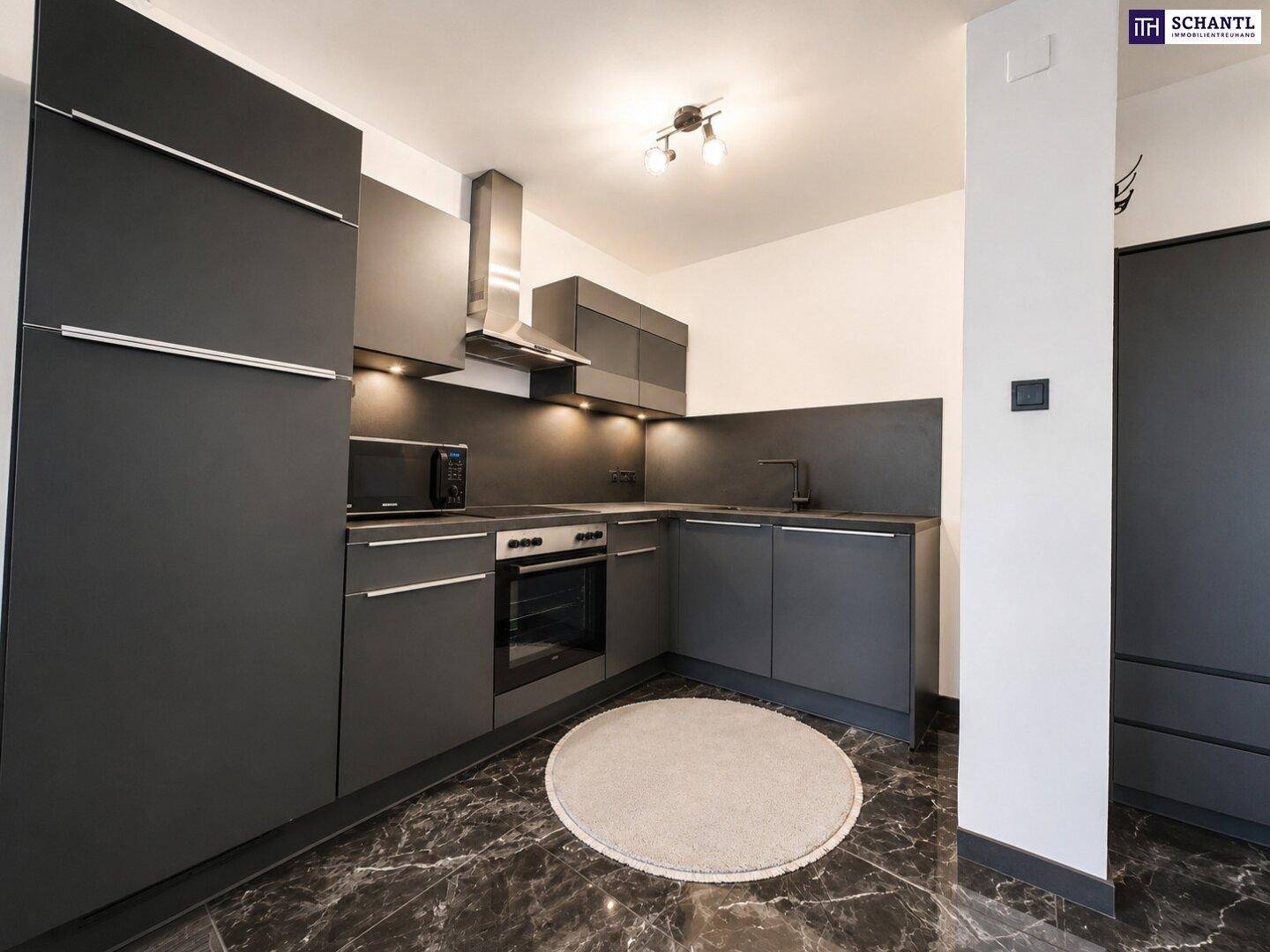 Moderne Küchenzeile in dunklem Grau mit integrierten Geräten und Steinboden.