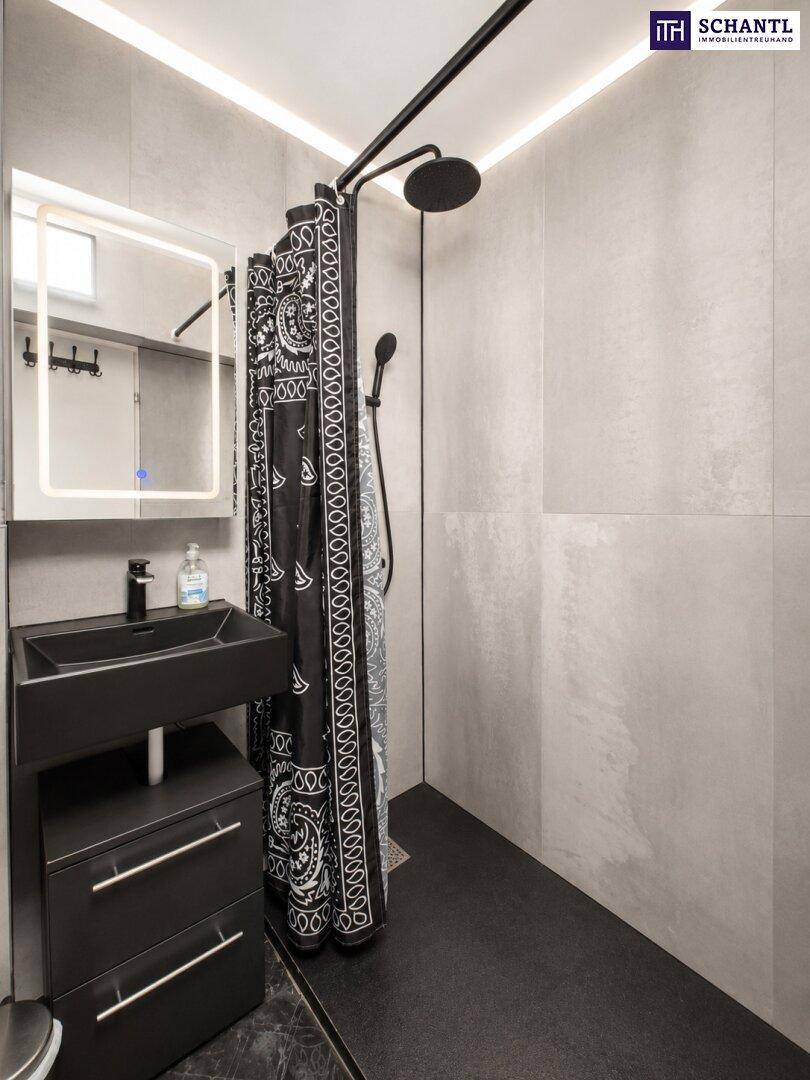 Modernes Badezimmer mit begehbarer Dusche, schwarzem Waschbecken und beleuchtetem Spiegelschrank.
