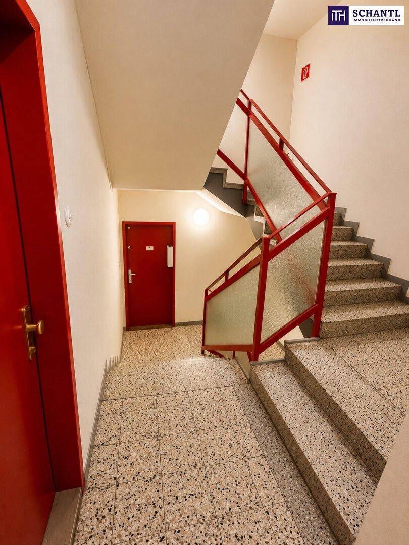 Treppenhaus mit Terrazzoboden, roten Geländern und Türen in einem Mehrfamilienhaus.