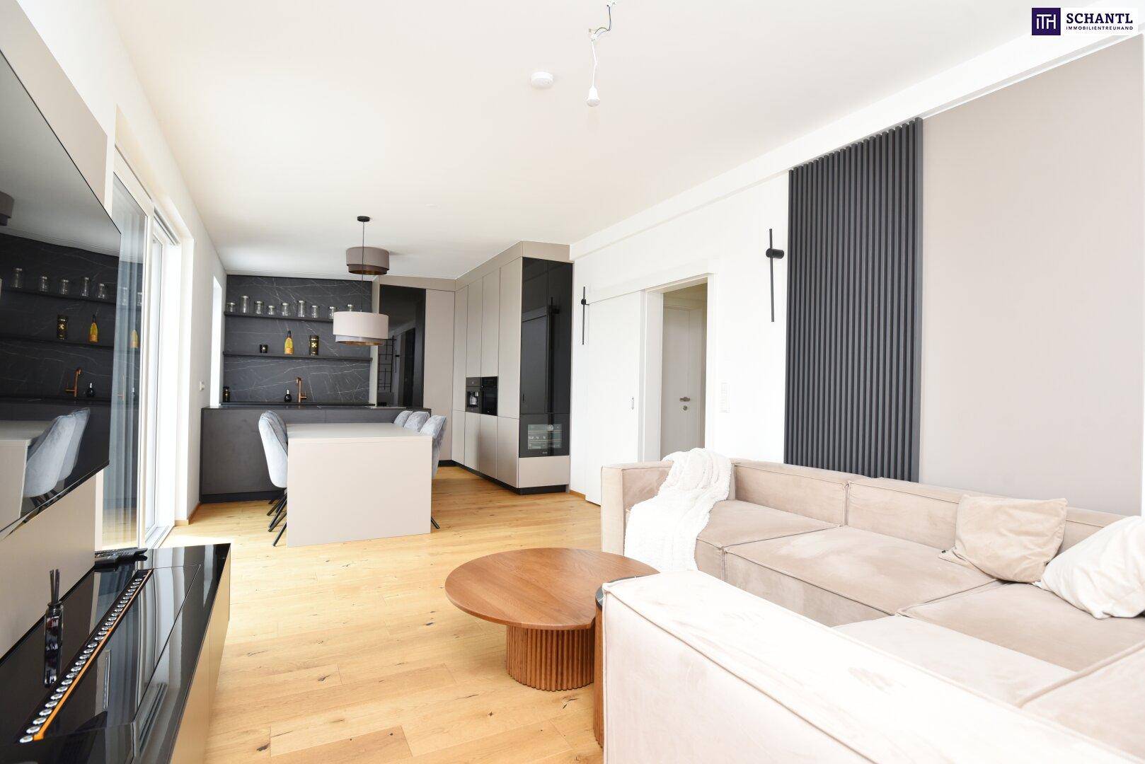 Offener Wohn-Essbereich mit moderner Küche, hellem Holzboden und beigem Sofa.