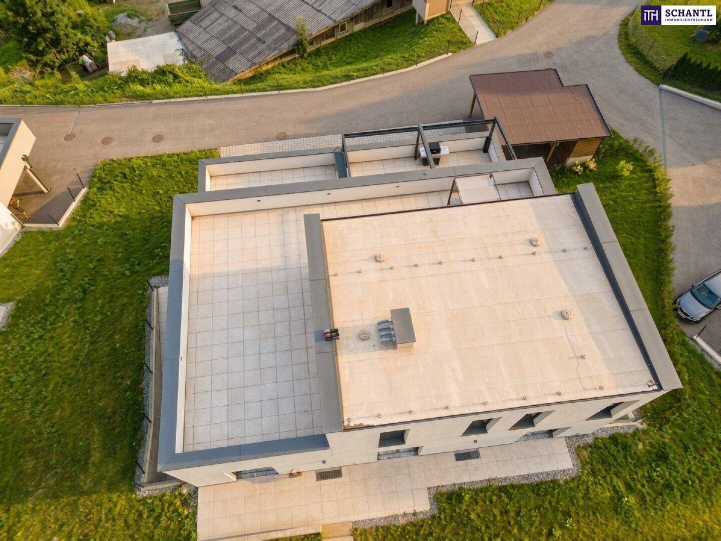 Luftaufnahme eines modernen Gebäudes mit großem Flachdach und weitläufiger Terrassenfläche.