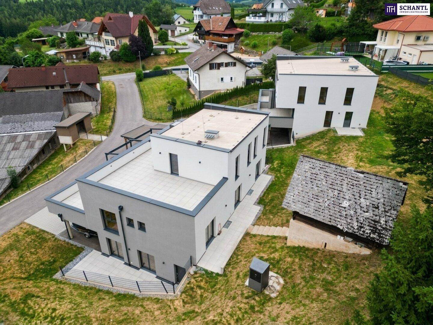 Luftaufnahme der modernen Wohnanlage mit zwei Gebäuden und einem historischen Holzschuppen.