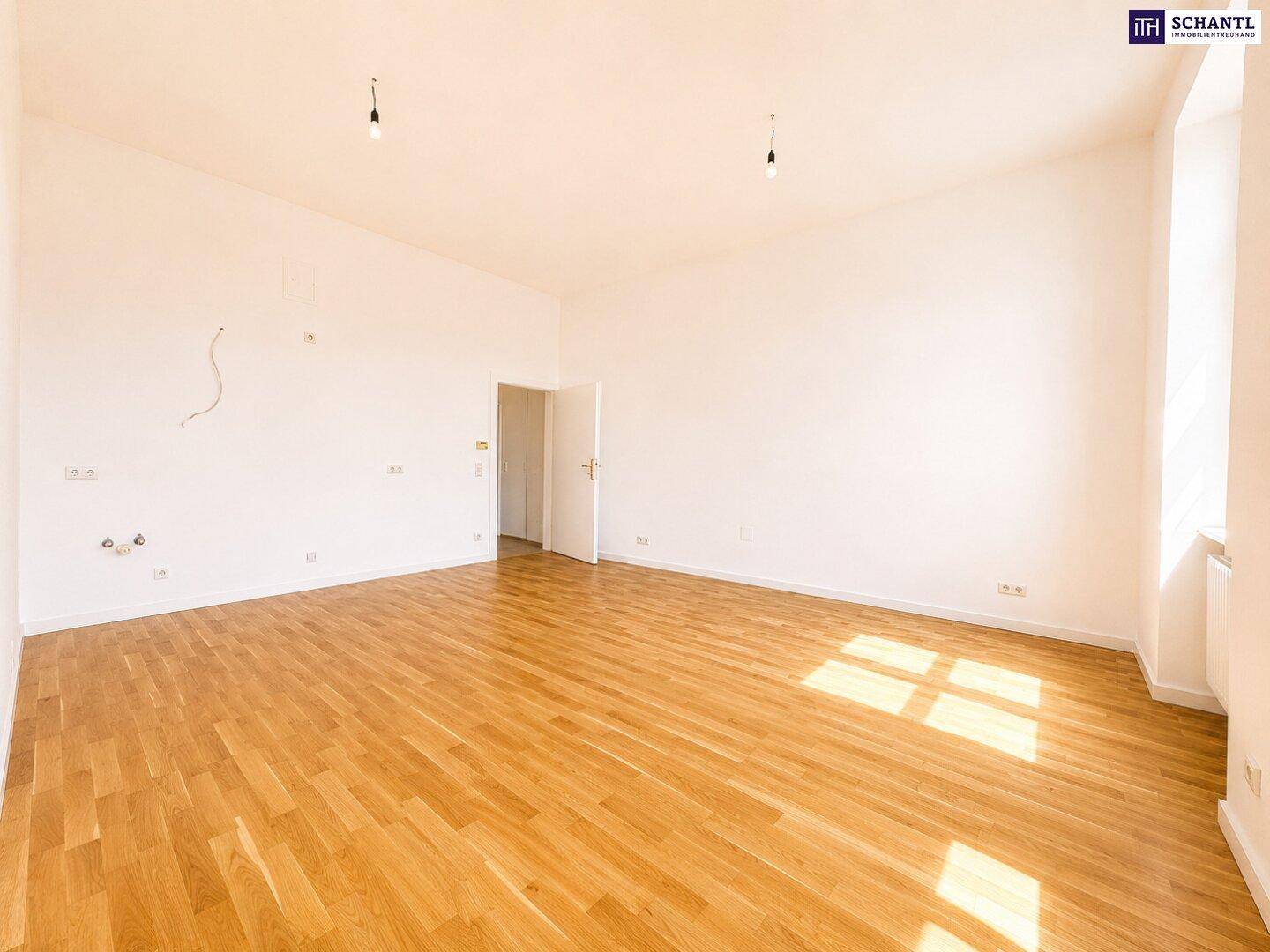 Heller, leerer Raum mit Holzboden und einer Tür, die zu einem weiteren Bereich der Wohnung führt.