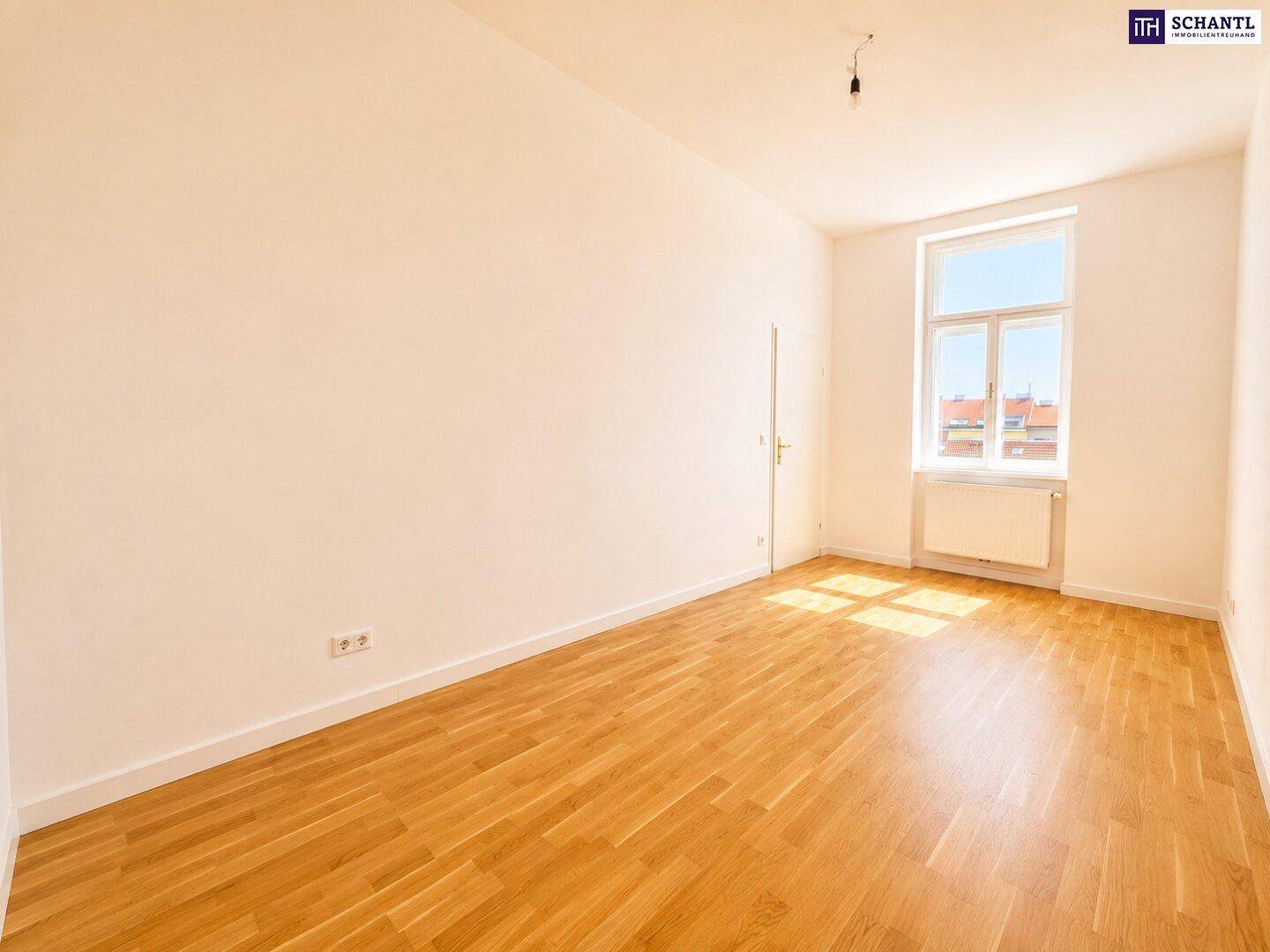 Langes, helles Zimmer mit Parkettboden und einem einzelnen Fenster, das viel Sonnenlicht spendet.