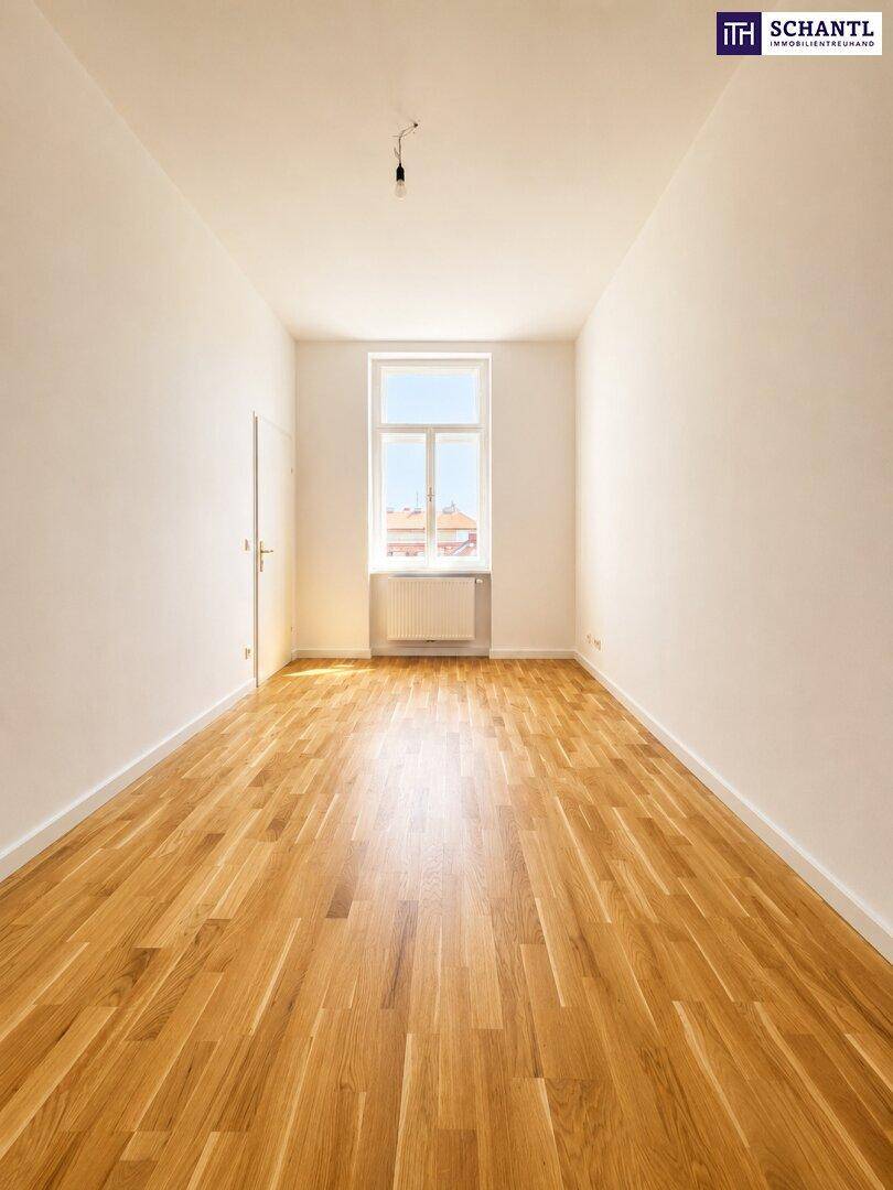 Schmaler, heller Raum mit Holzboden und einem hohen Fenster, das den Raum mit Licht erfüllt.