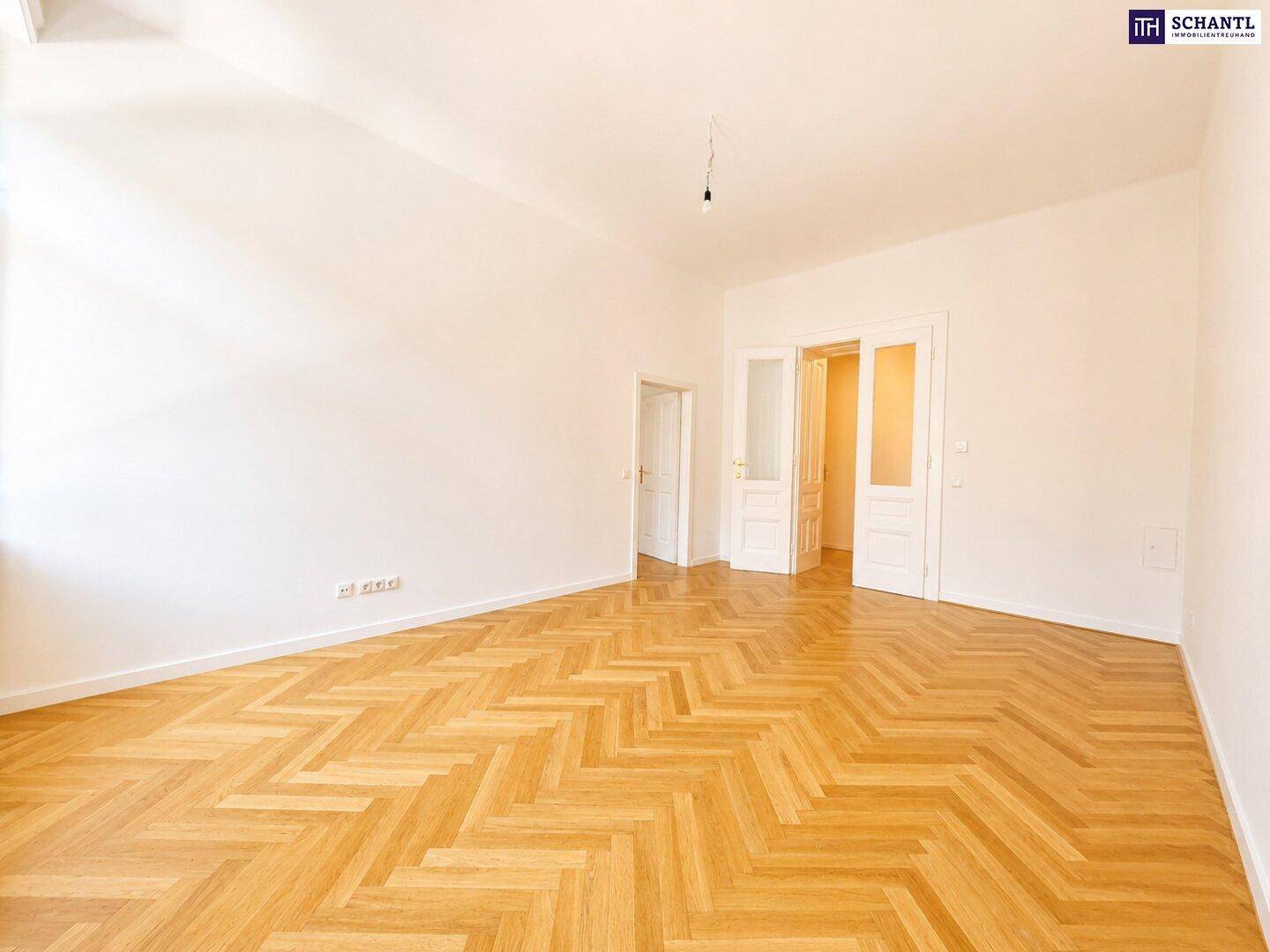 Heller Raum mit Fischgrätparkett und zwei offenen Türen, die den Blick in weitere, ähnlich gestaltete Zimmer freigeben.