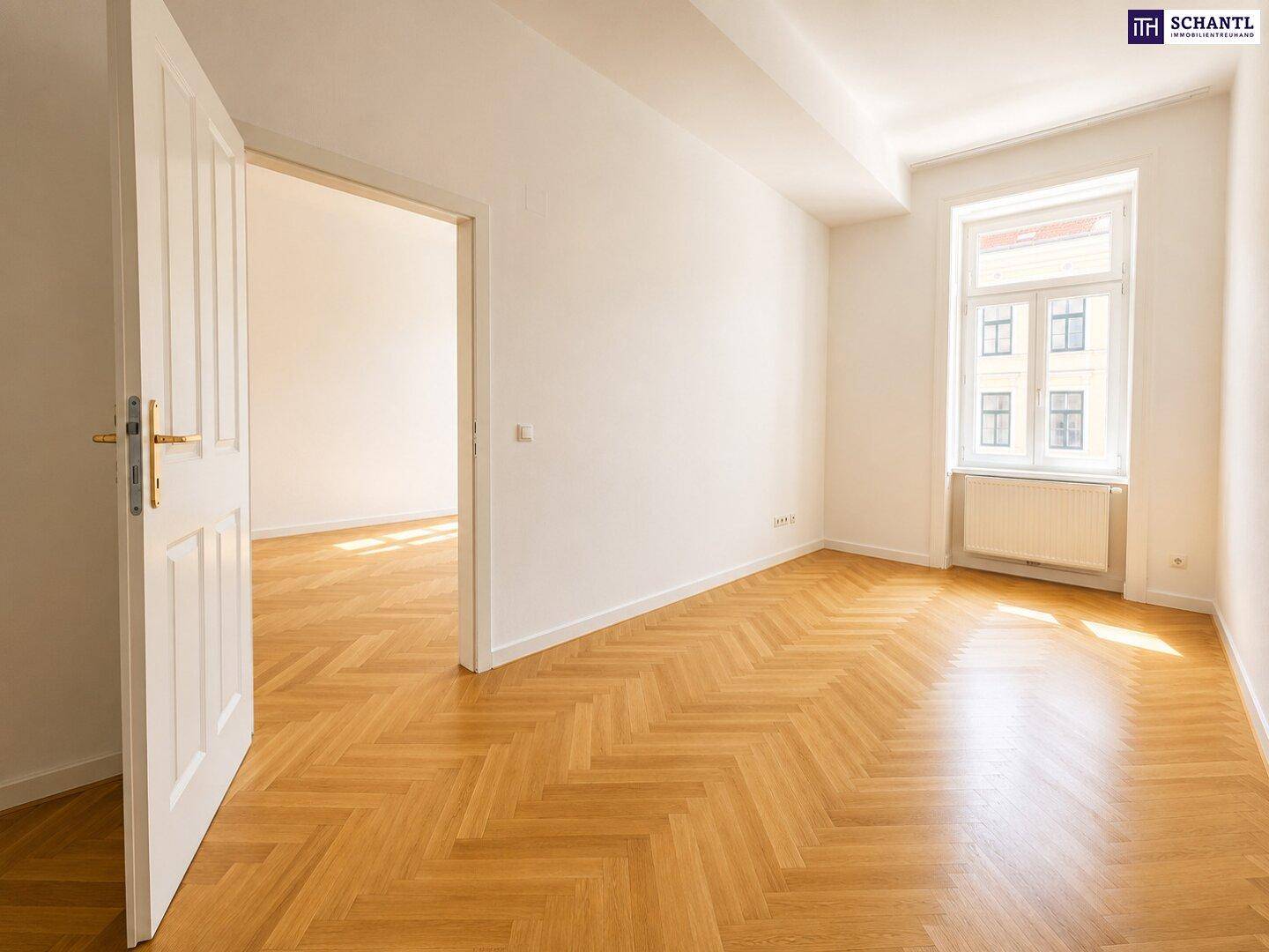 Ruhiges Zimmer mit Fischgrätparkett, einem großen Fenster und Zugang zu einem weiteren hellen Raum.