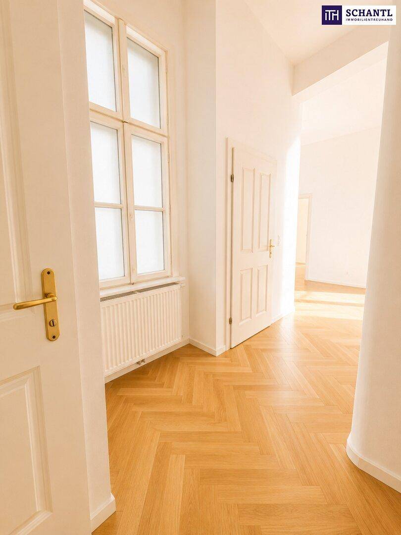 Heller Flur mit Fischgrätparkettboden, einem Fenster und einer offenen Tür, die zu weiteren Räumen führt.