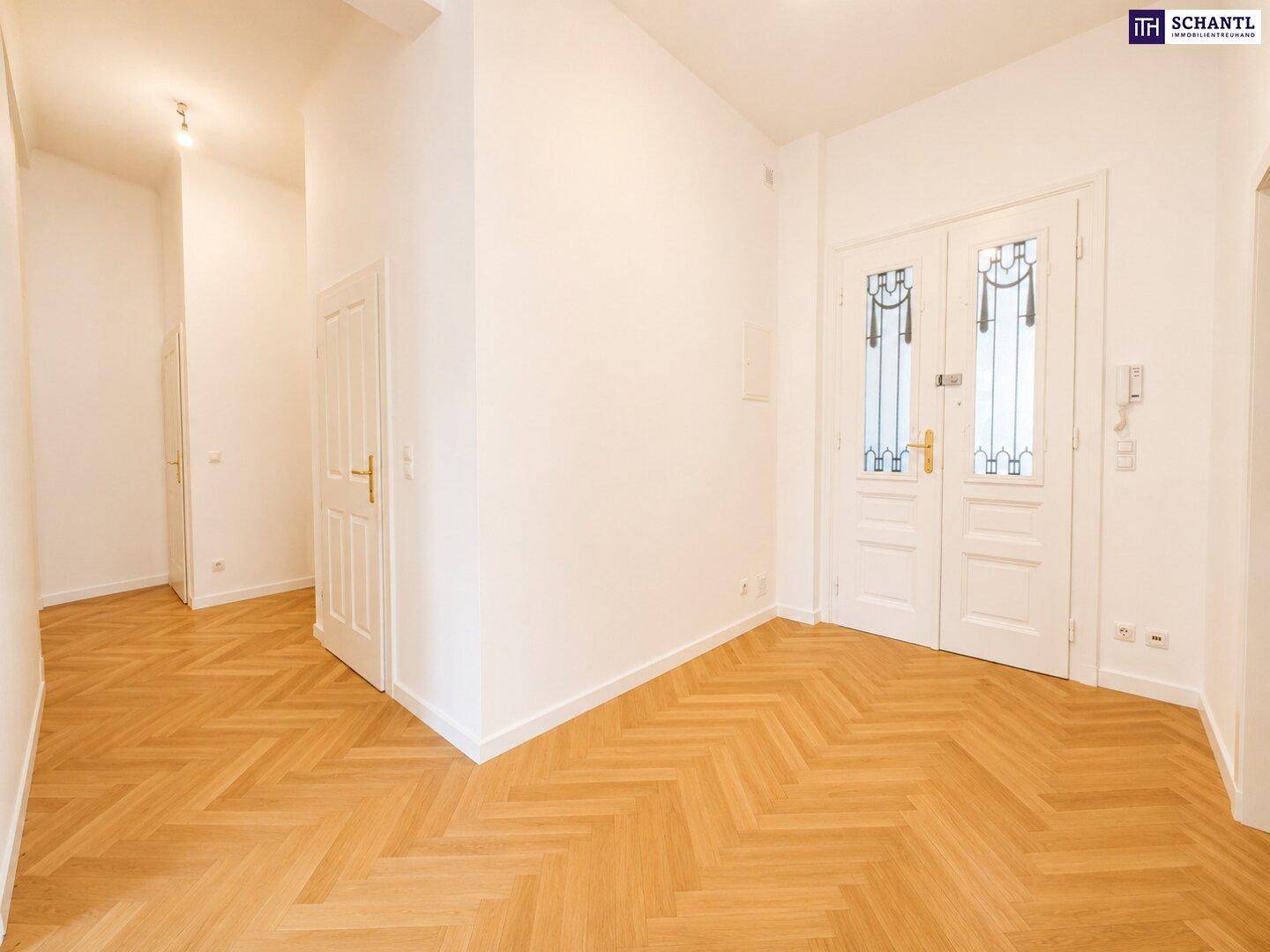 Eleganter Flur mit Fischgrätparkett und einer verzierten Doppeltür, die den Eingangsbereich prägt.