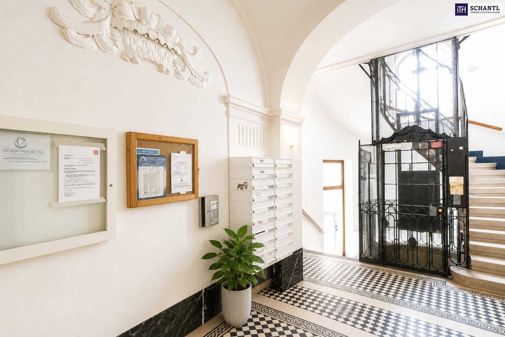 Heller Eingangsbereich mit Briefkästen, dekorativer Decke und Blick auf den historischen Aufzug und die Treppe.