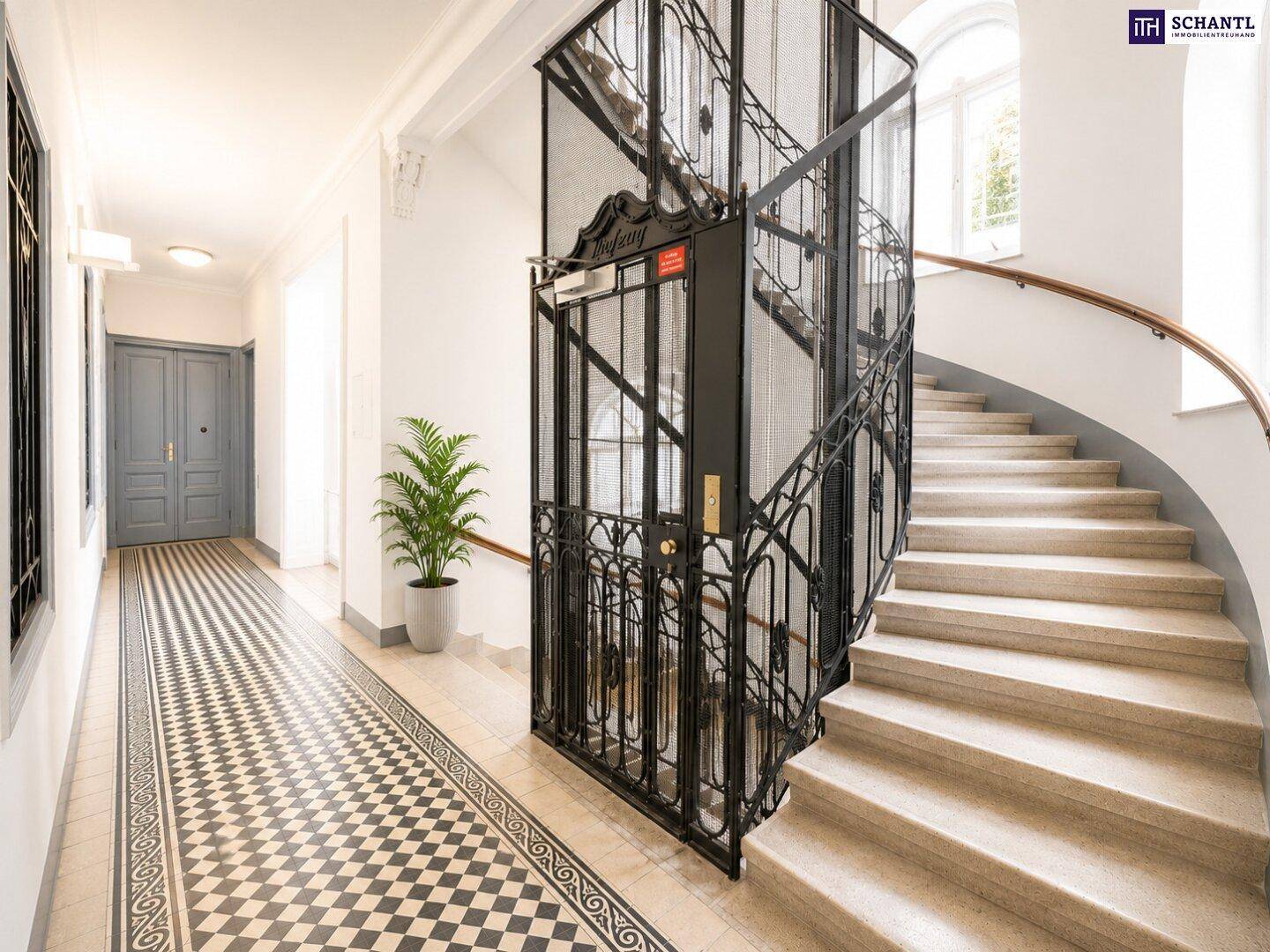 Prunkvoller Eingangsbereich mit historischem Aufzug, eleganter Treppe und gemustertem Fliesenboden.