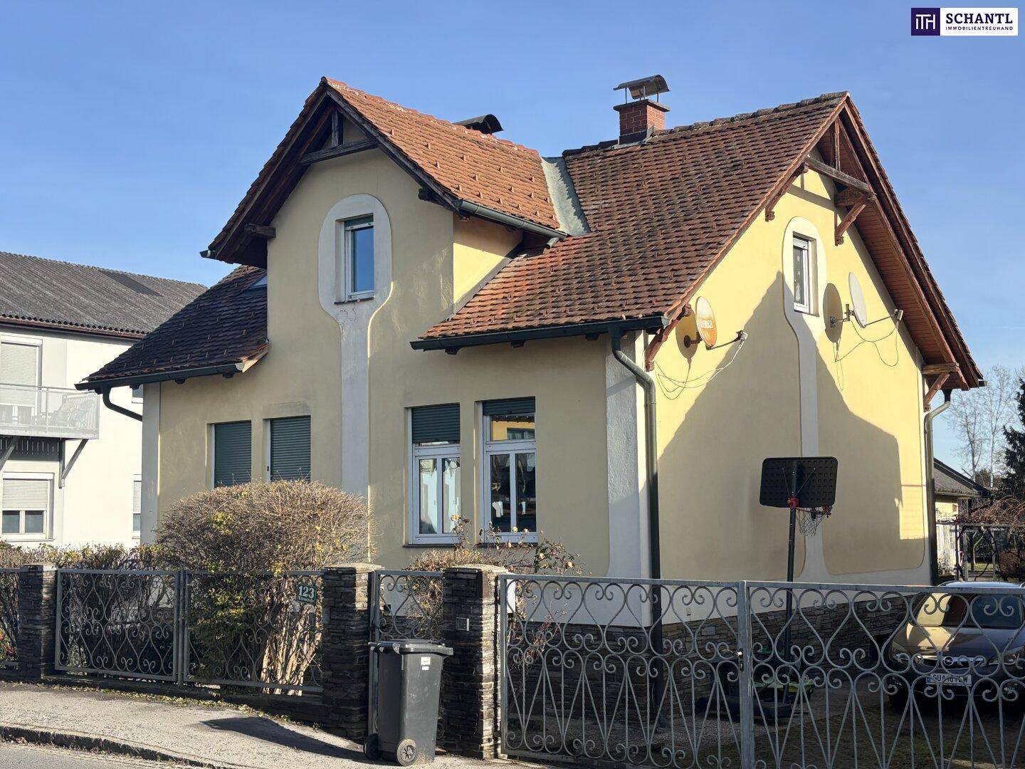 Seitenansicht des gelben Hauses mit Ziegeldach und Satellitenschüsseln.