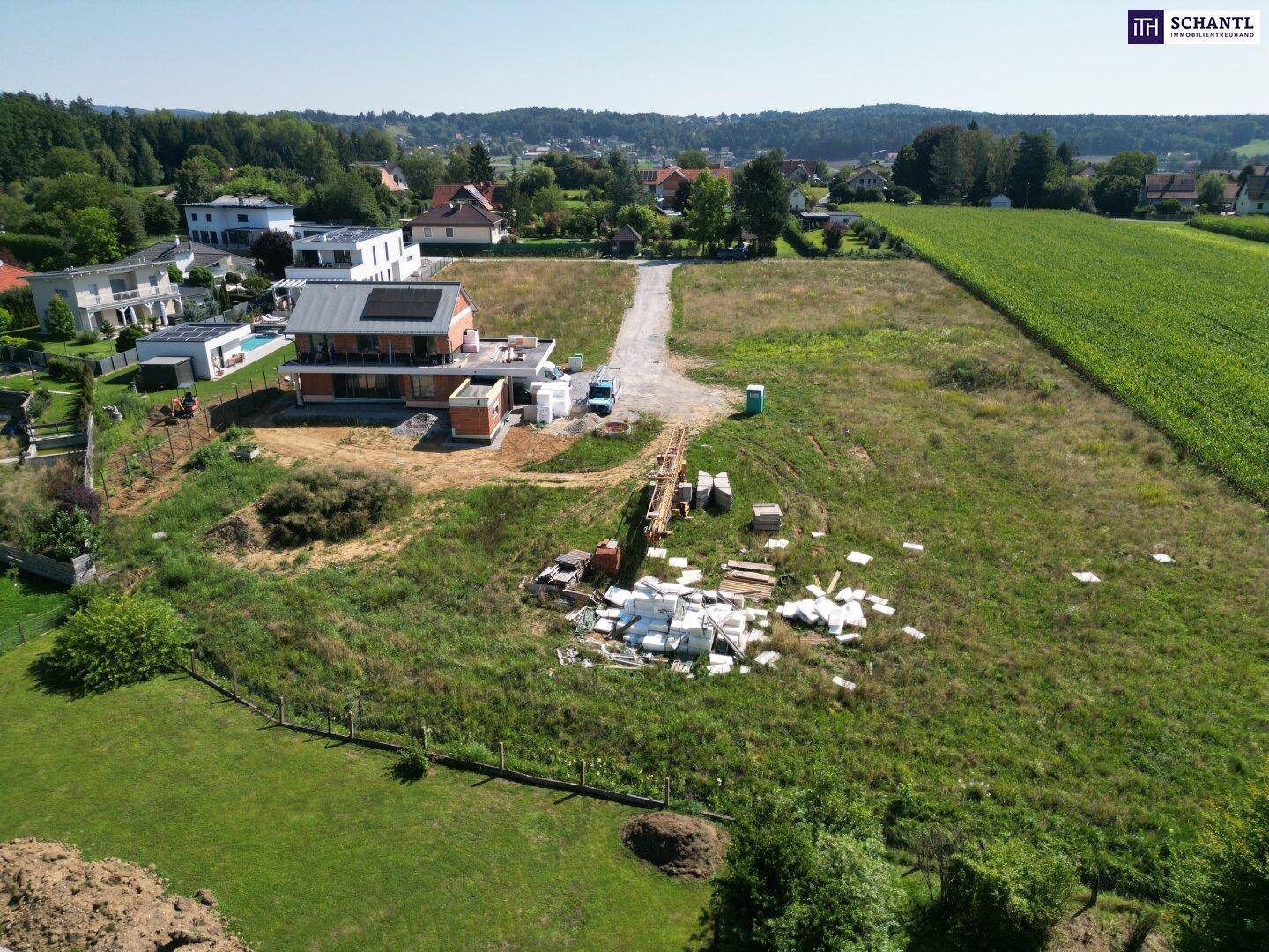 Luftaufnahme einer Baustelle mit einem im Bau befindlichen Haus, umgeben von Feldern und Wohnhäusern.