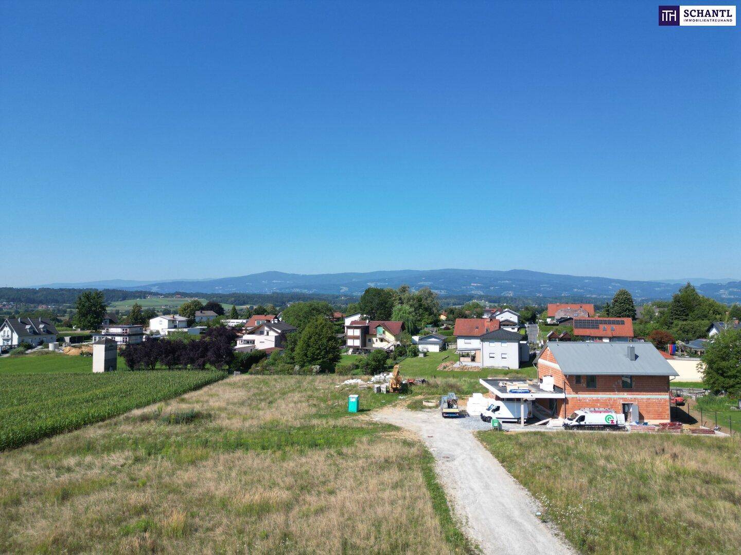 Weitläufige Luftaufnahme einer Baustelle mit einem Neubau und Blick auf die umliegende Landschaft und Berge.