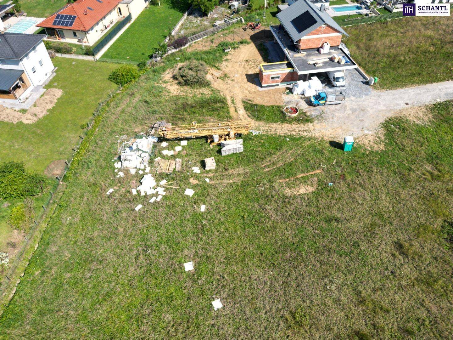 Luftaufnahme einer Baustelle mit einem fast fertigen Haus und weiteren Wohnhäusern in der ländlichen Umgebung.