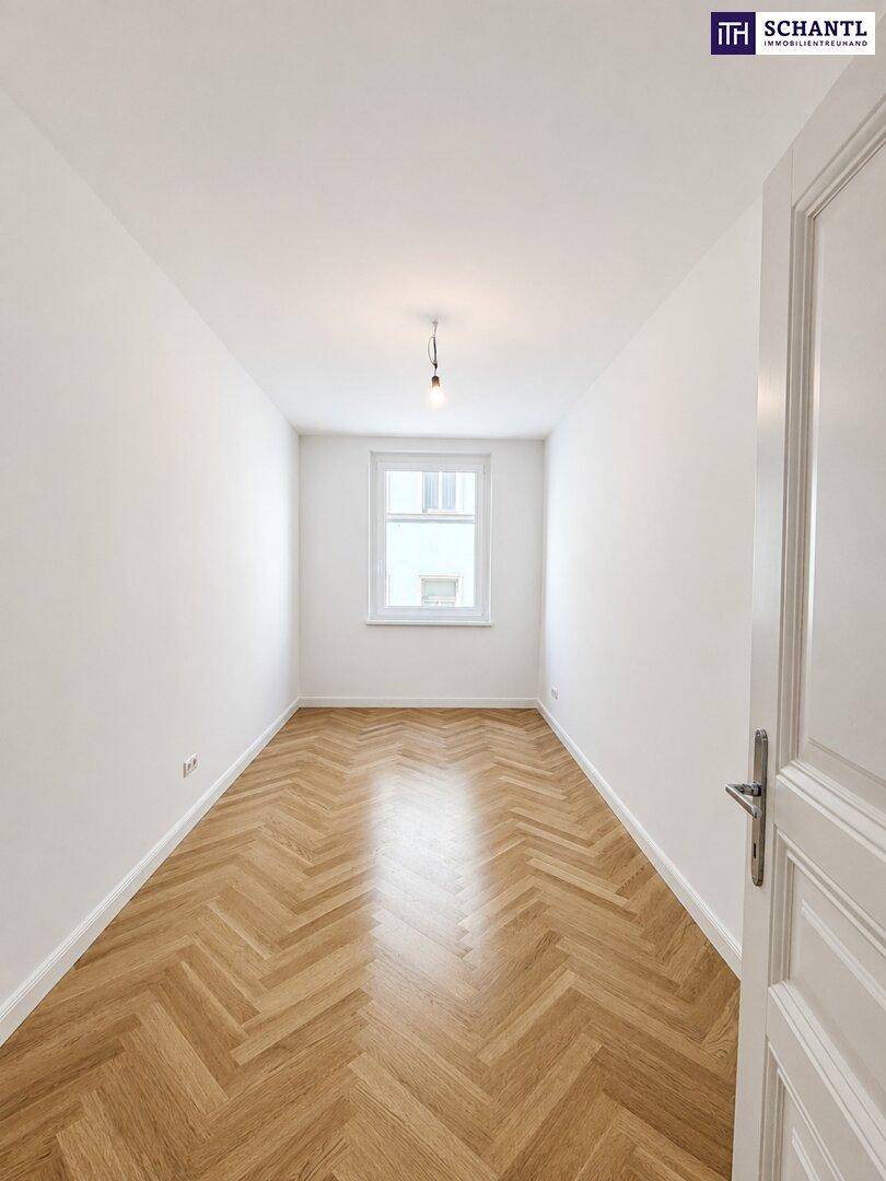 Langer, heller Raum mit klassischem Fischgrätparkett und einem Fenster, das Tageslicht hereinlässt.