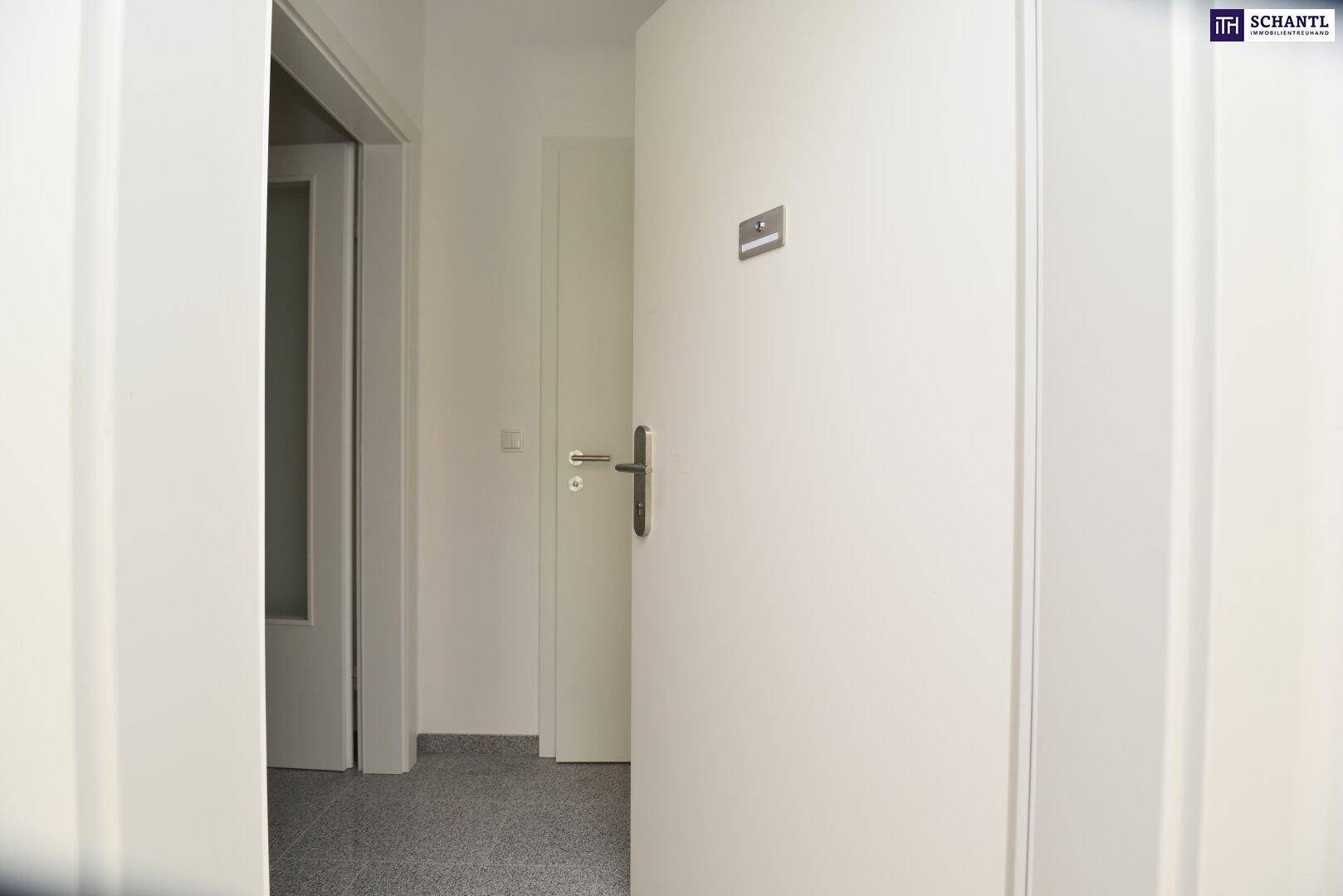 Heller Flur mit weißer Tür und grauen Fliesen, der zu weiteren Räumen führt.