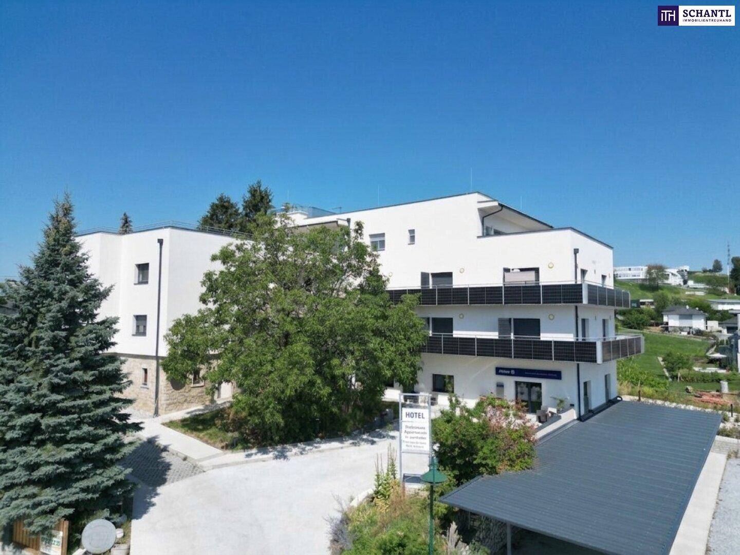 Modernes Gebäude mit weißen Fassaden, Balkonen und Carport, eingebettet in grüne Umgebung.