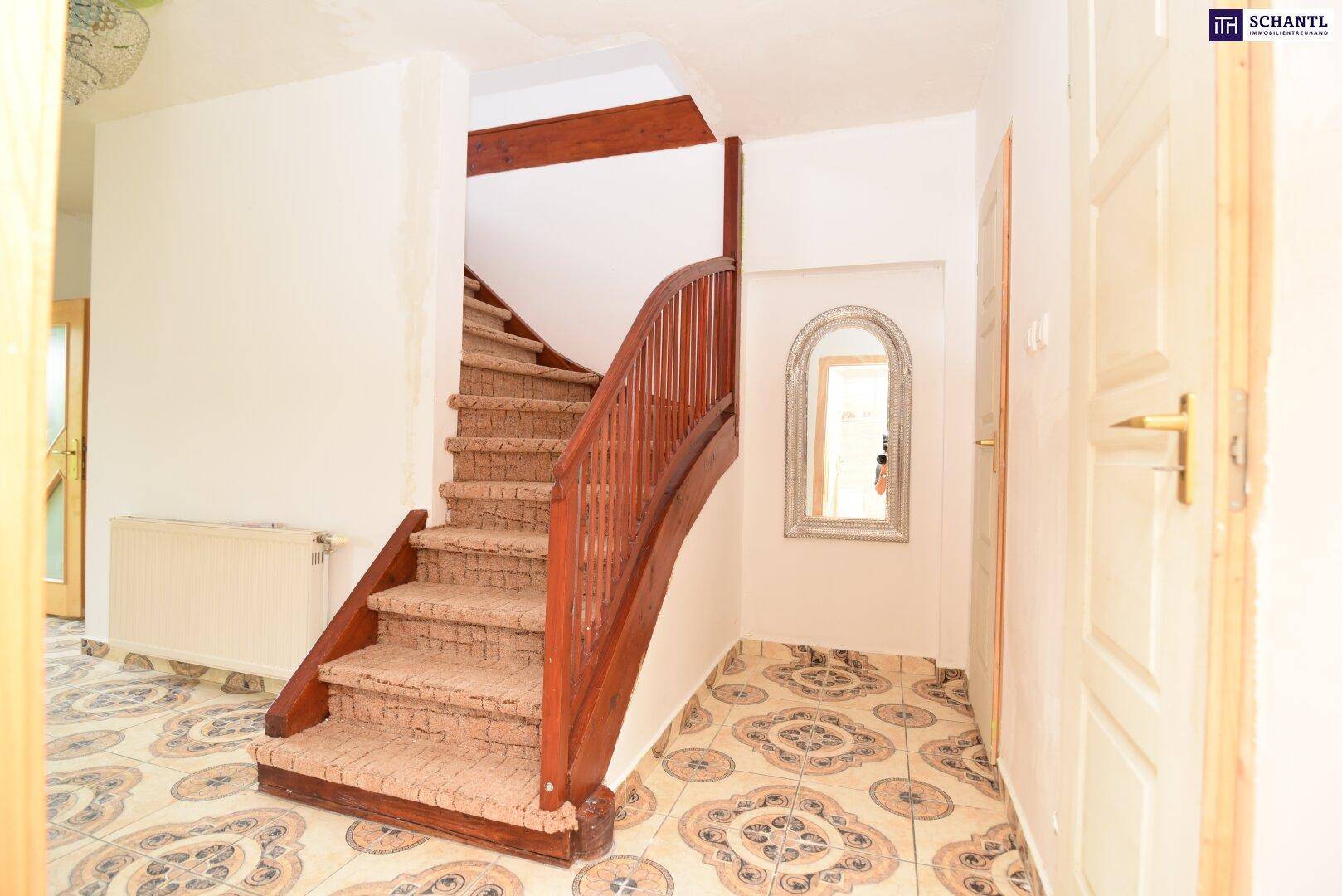 Eingangsbereich mit einer Holztreppe, gemusterten Fliesen und einem kleinen Spiegel an der Wand.