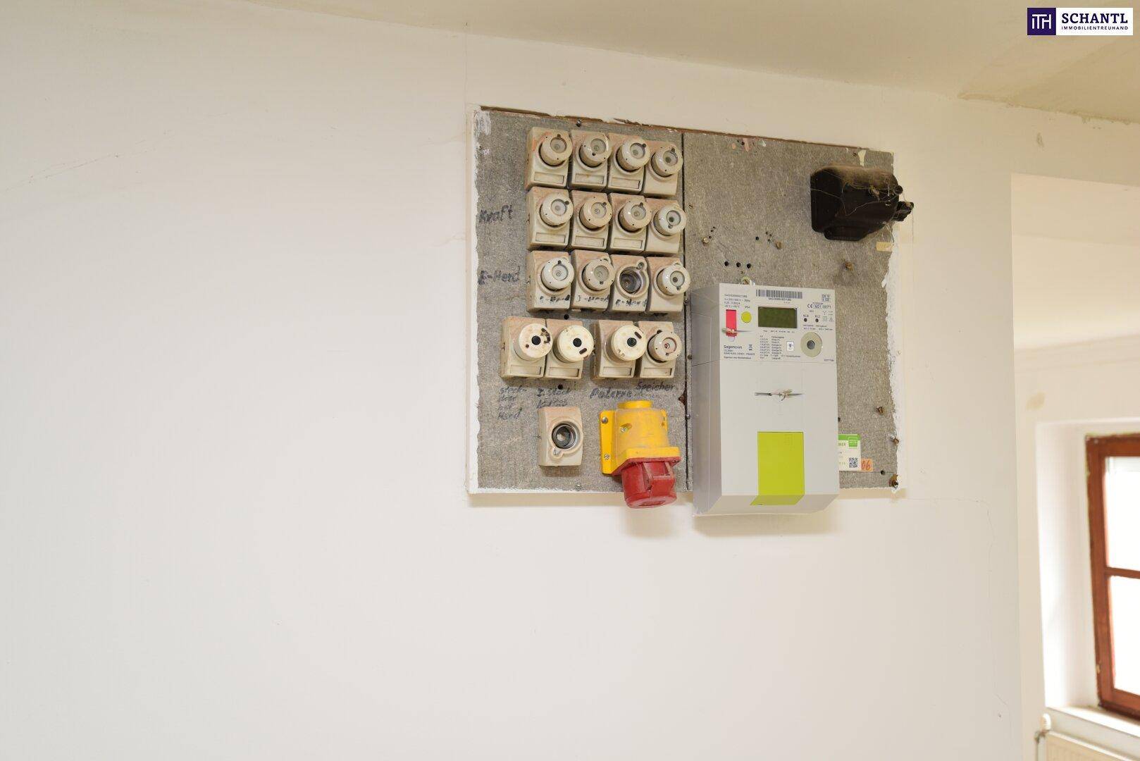 Elektrischer Sicherungskasten und Zähler an einer weißen Wand mit einem Fensterrahmen.