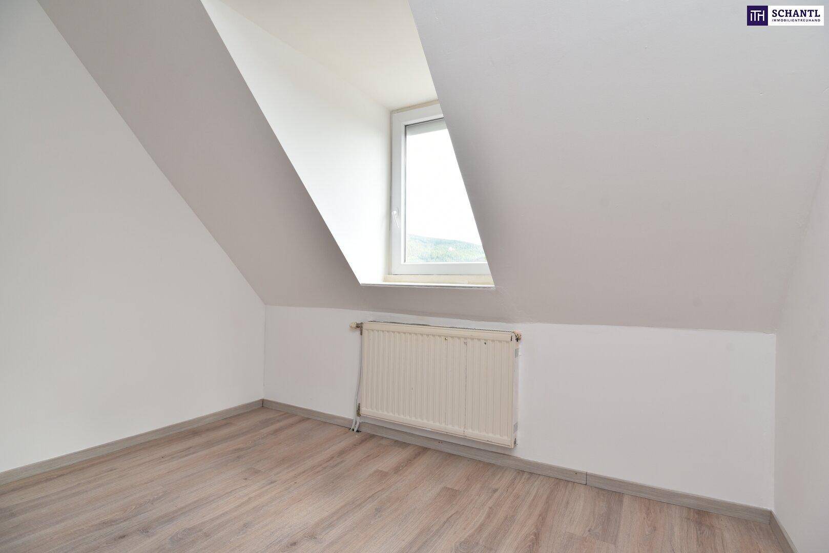 Leerer Raum im Dachgeschoss mit schrägen Wänden, Laminatboden und einem Fenster für Tageslicht.