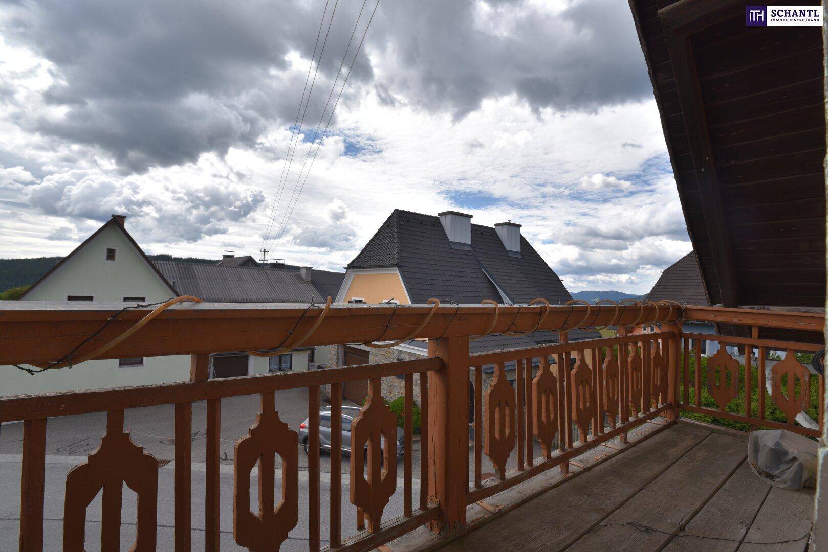 Balkon mit traditionellem Holzgeländer und Blick auf die umliegende Wohngegend unter bewölktem Himmel.