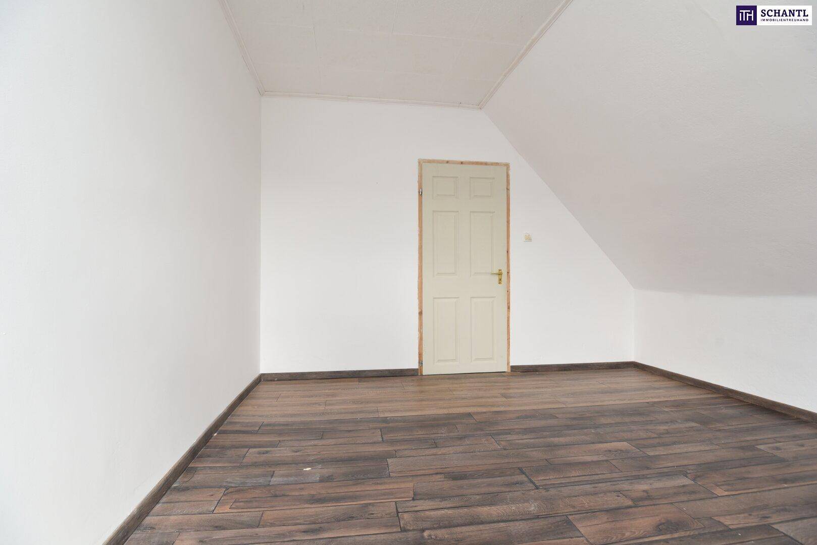 Leeres Dachgeschosszimmer mit dunklem Holzboden, weißen Wänden und einer einfachen Holztür.