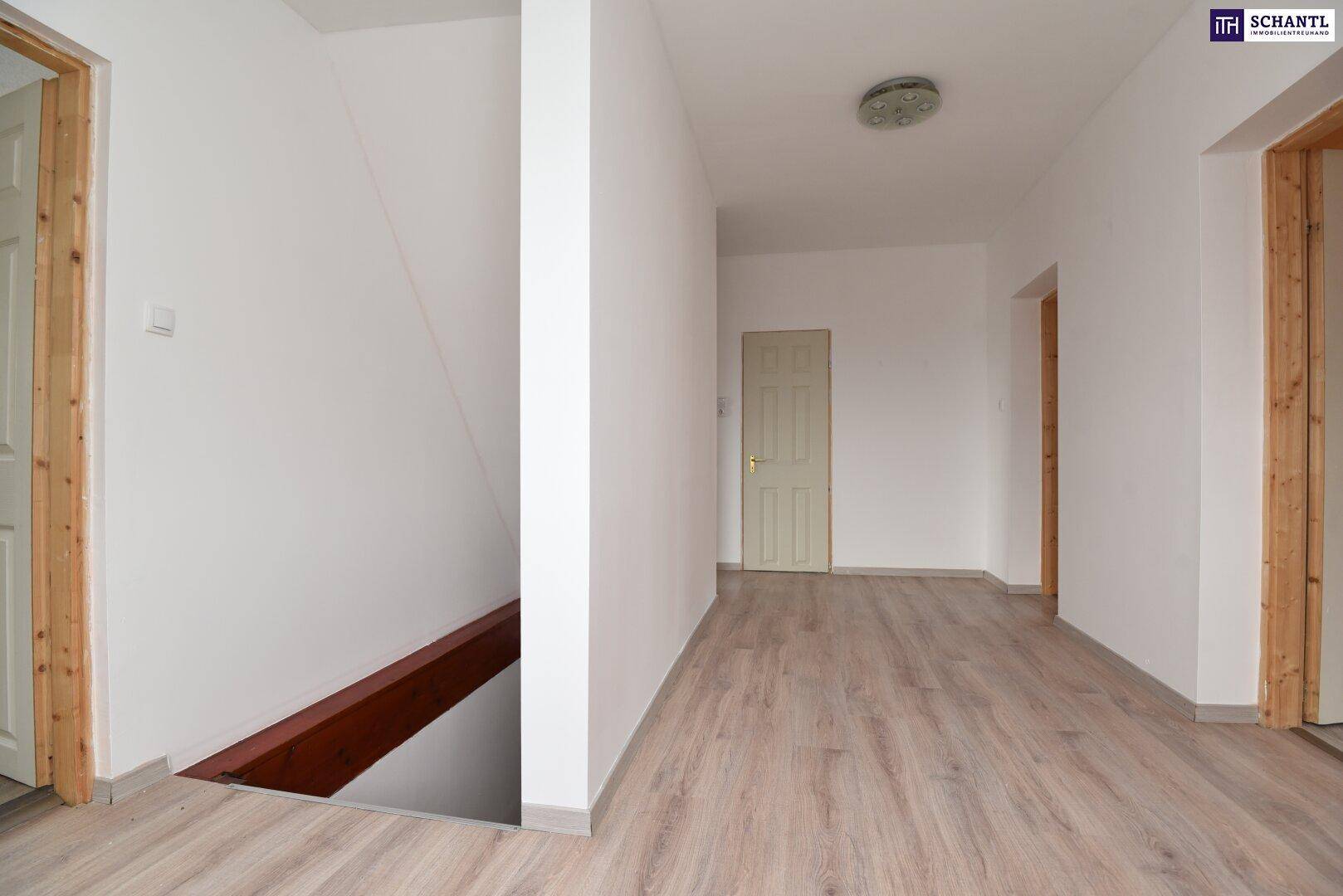 Heller Flur mit Laminatboden, weißen Wänden und Holztürrahmen, der zu weiteren Räumen führt.